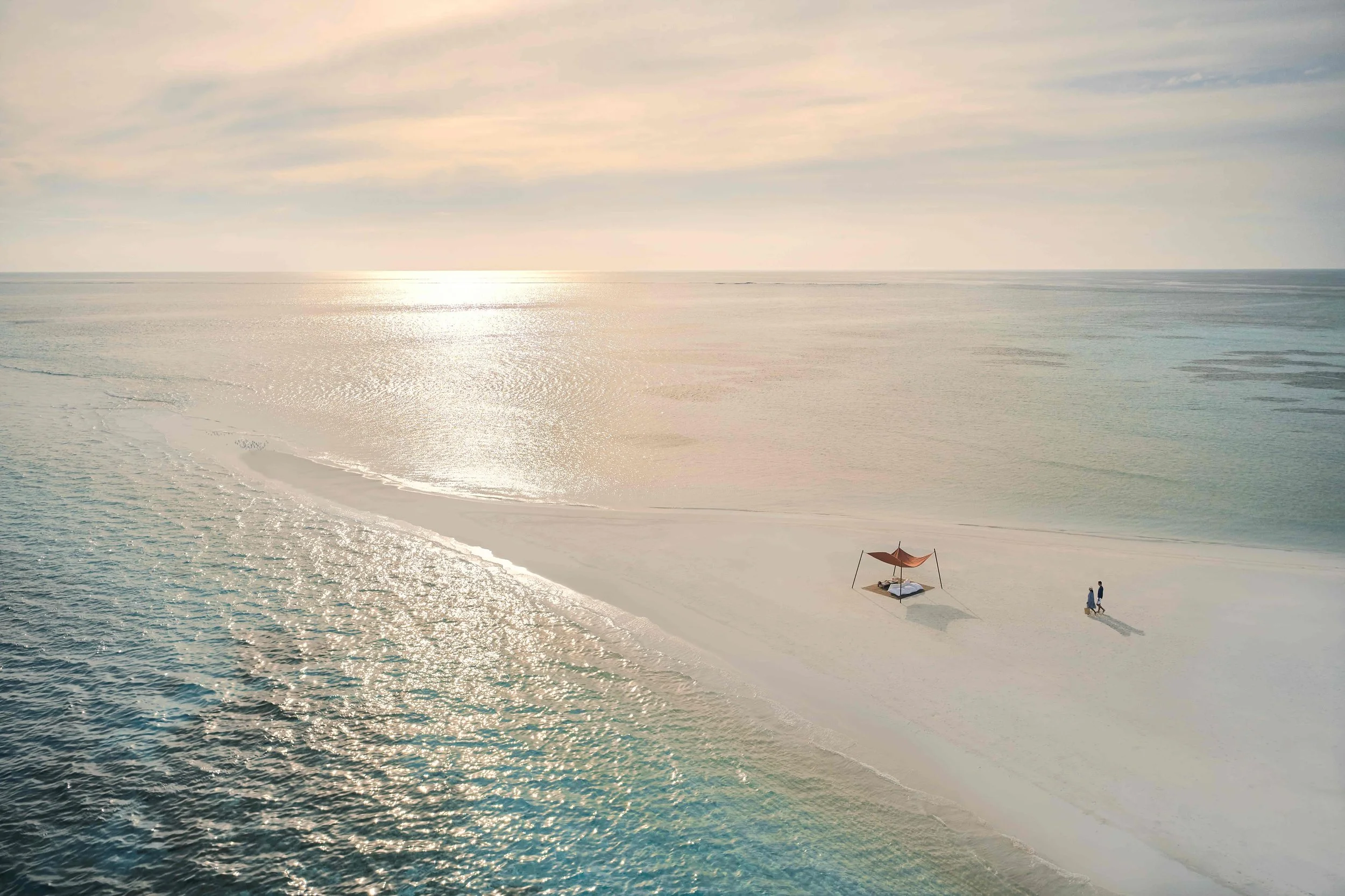 Aerial photo of a couple walking towards a private sandbank set-up at sunset