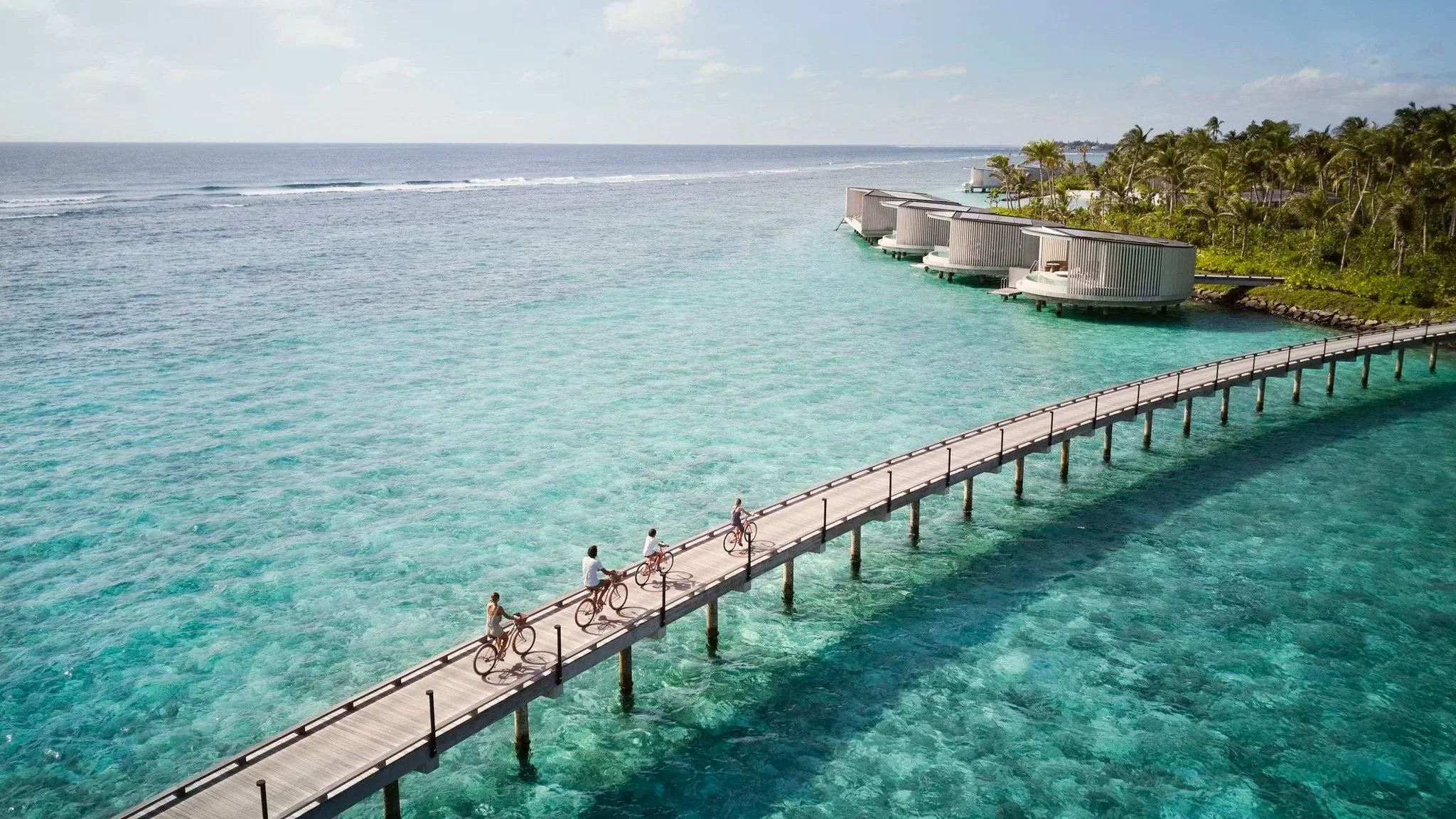 Family riding bikes across a bridge to an island near water villas