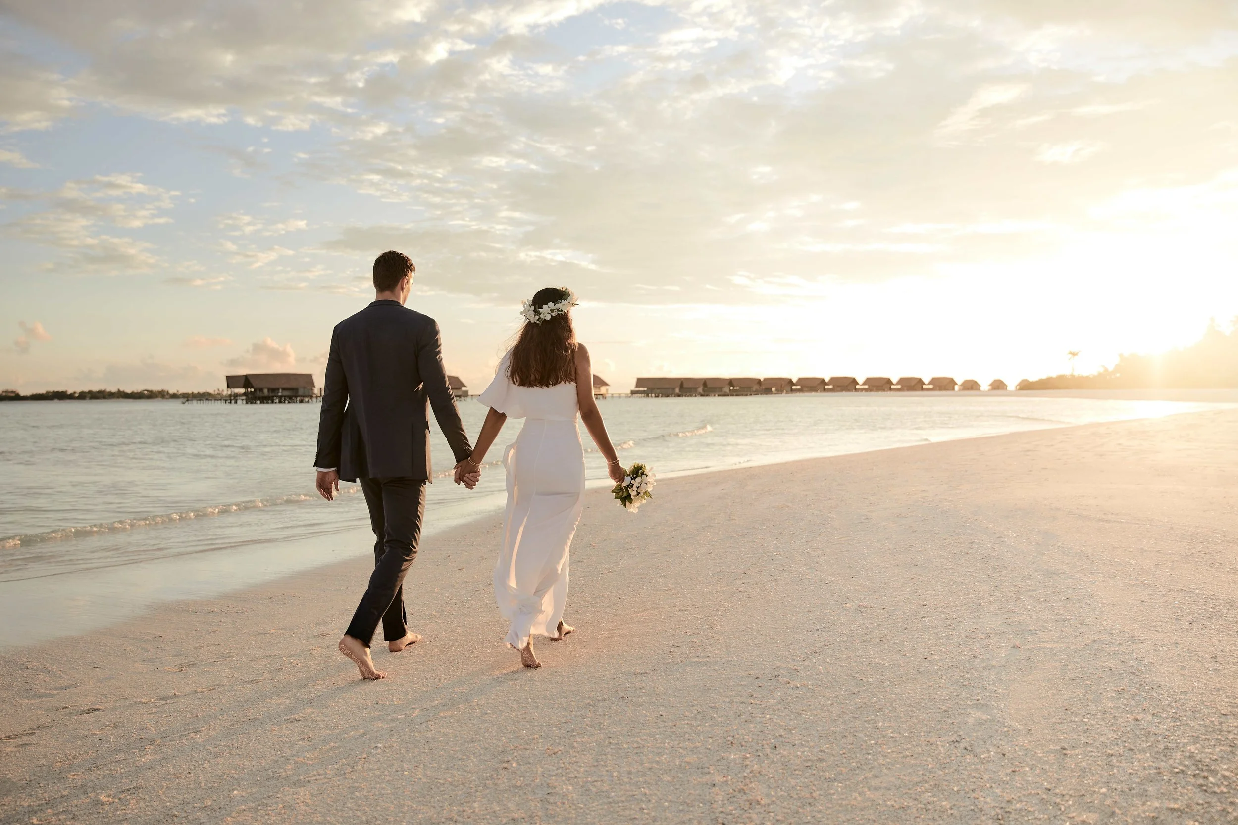 Wedding couple walking on a beach with water villas in the background