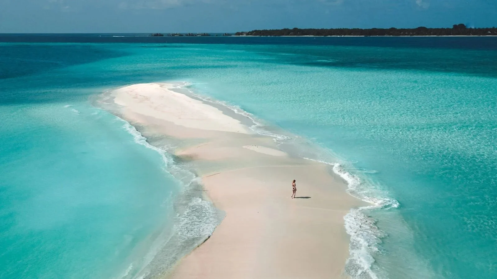 Woman walking on a sandbank with Soneva Fushi Resort in the background