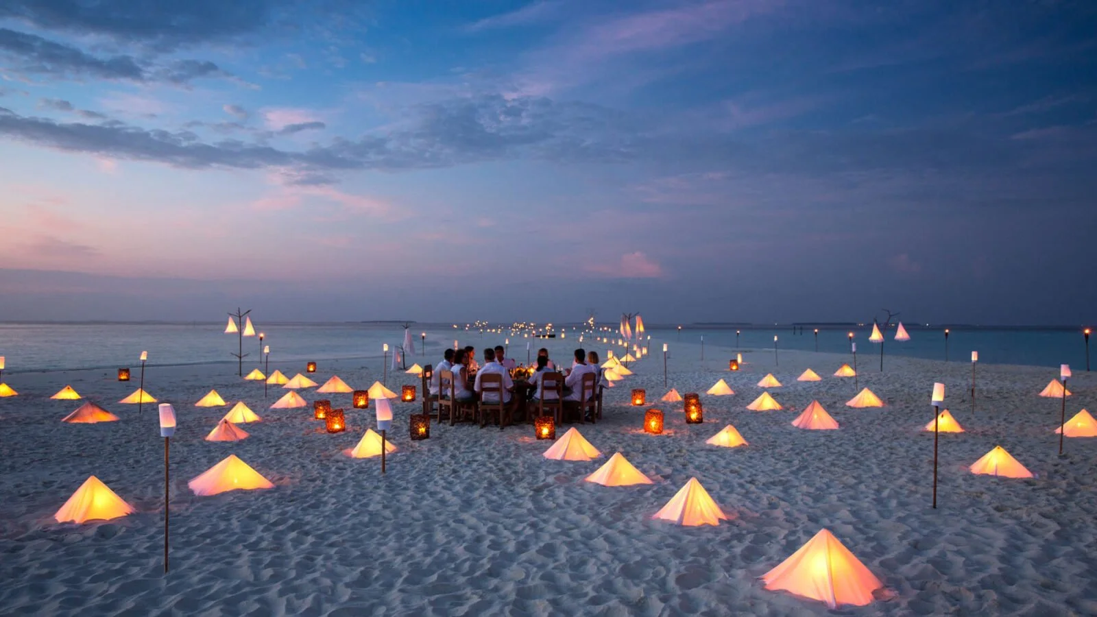 round table with people surrounded by lights on a sandbank at sunset