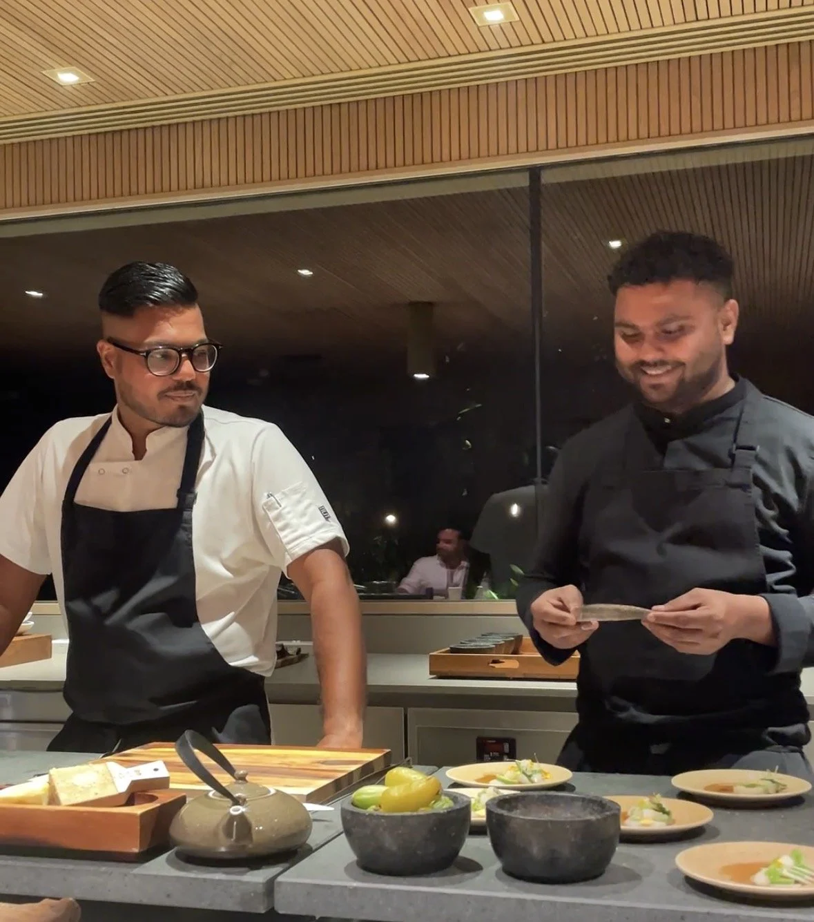Two chefs in front of a chefs table serving food