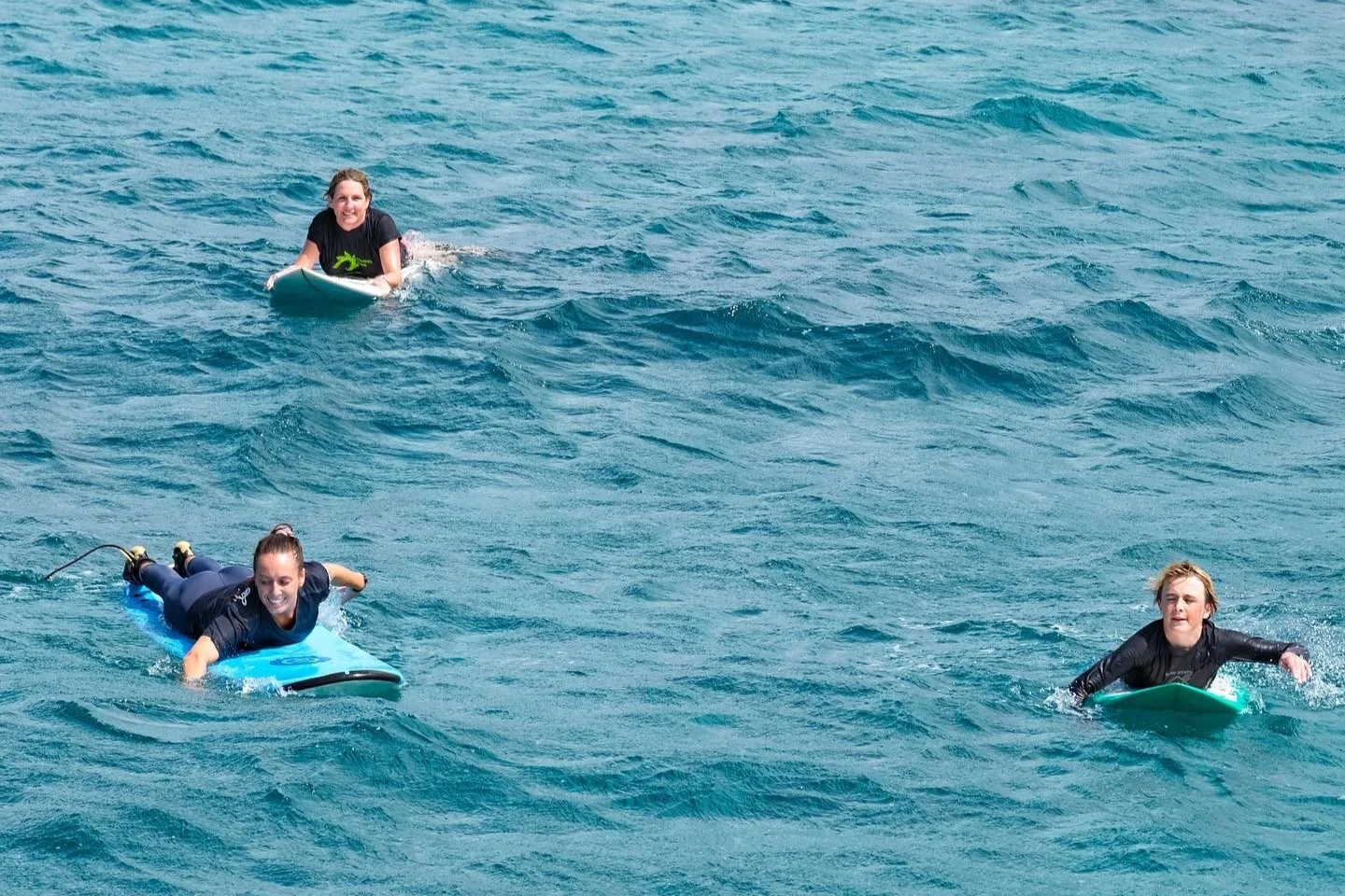 Three people in the water on surfboards paddling