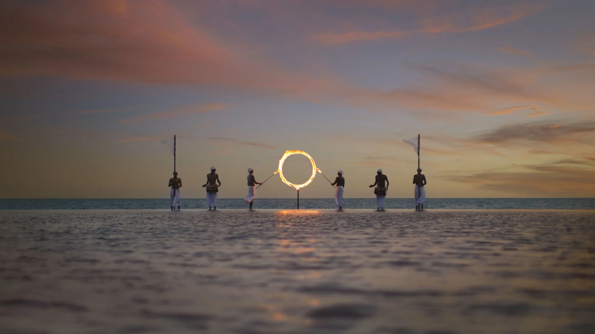 Maldivians standing on the edge of the pool holding flags and a ring of fir4e