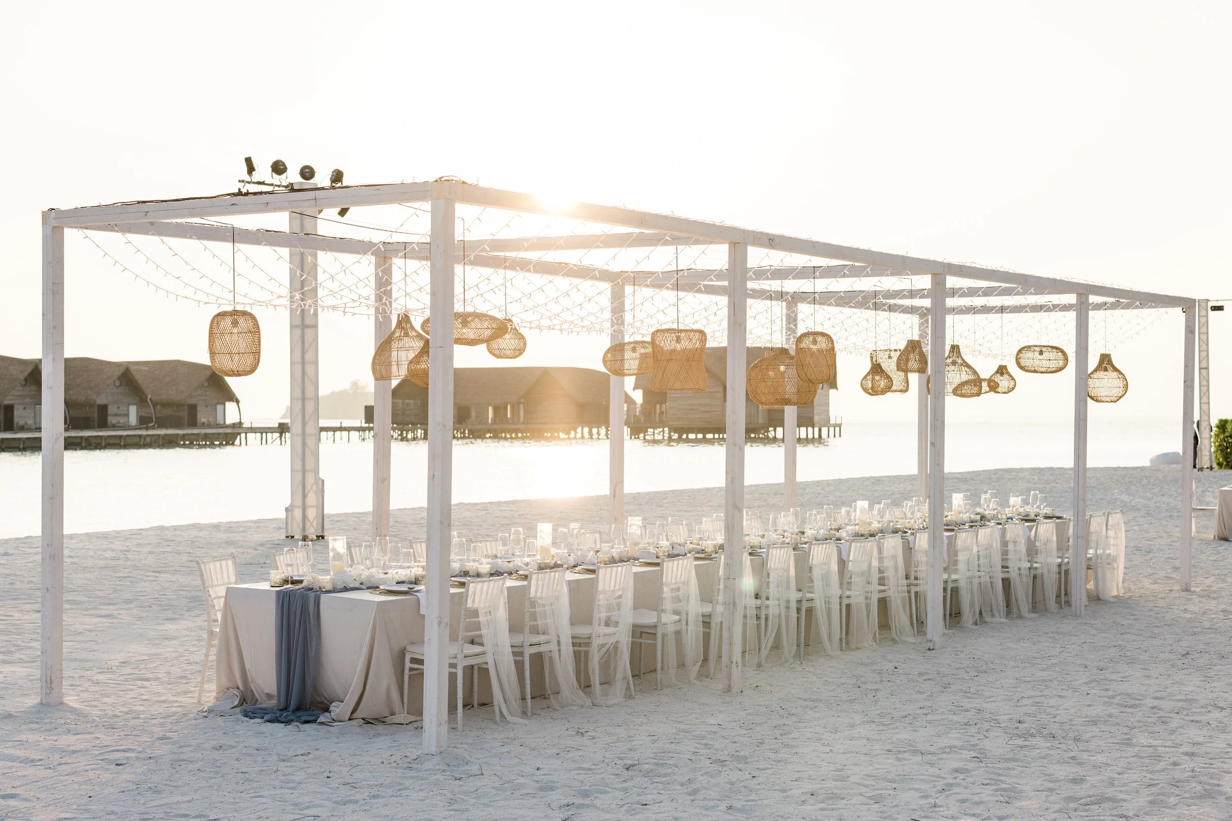 White table decorated set on the beach looking at water villas