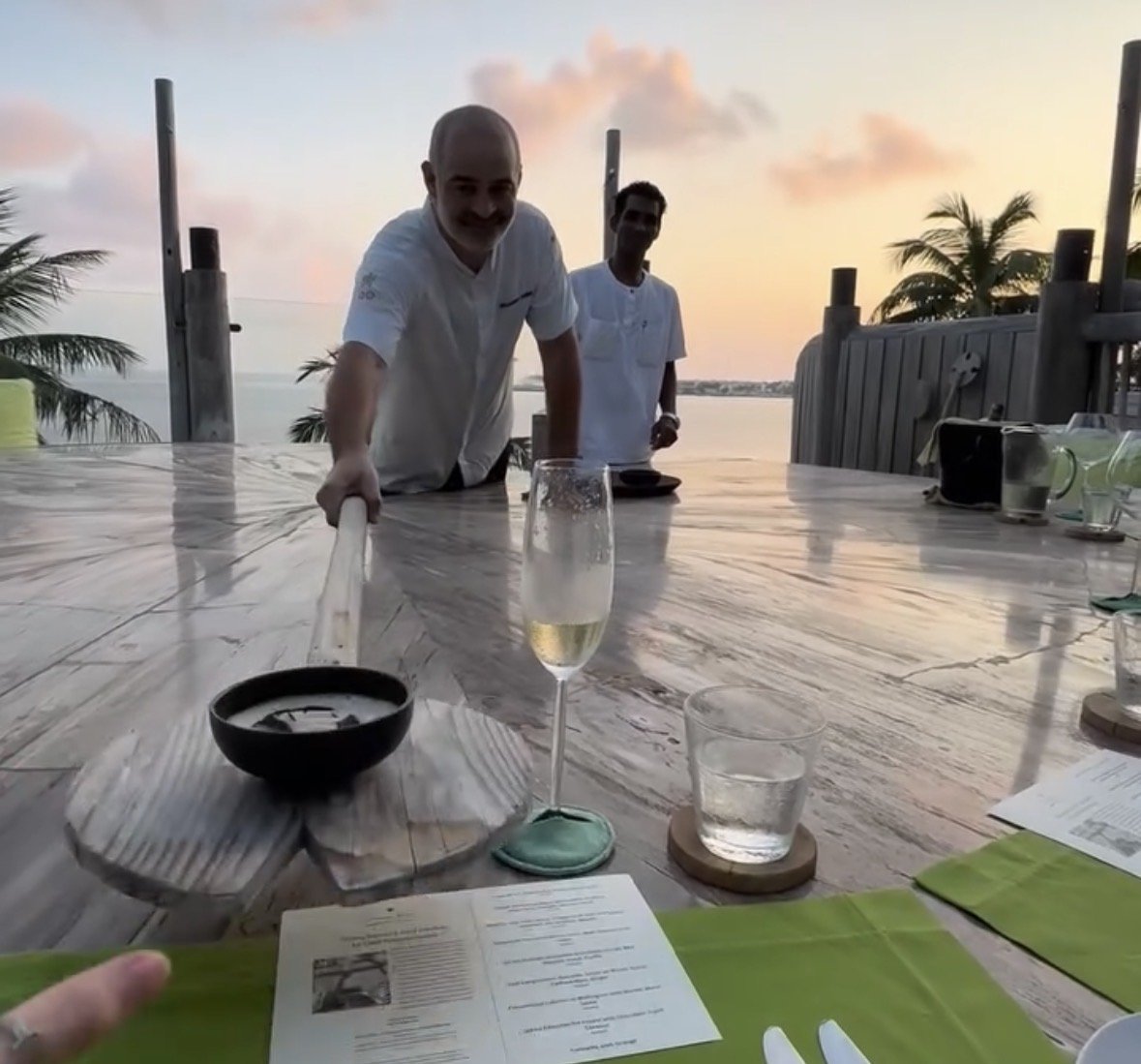 Chef serving Jodie Mason at a sunset table with a glass of champagne