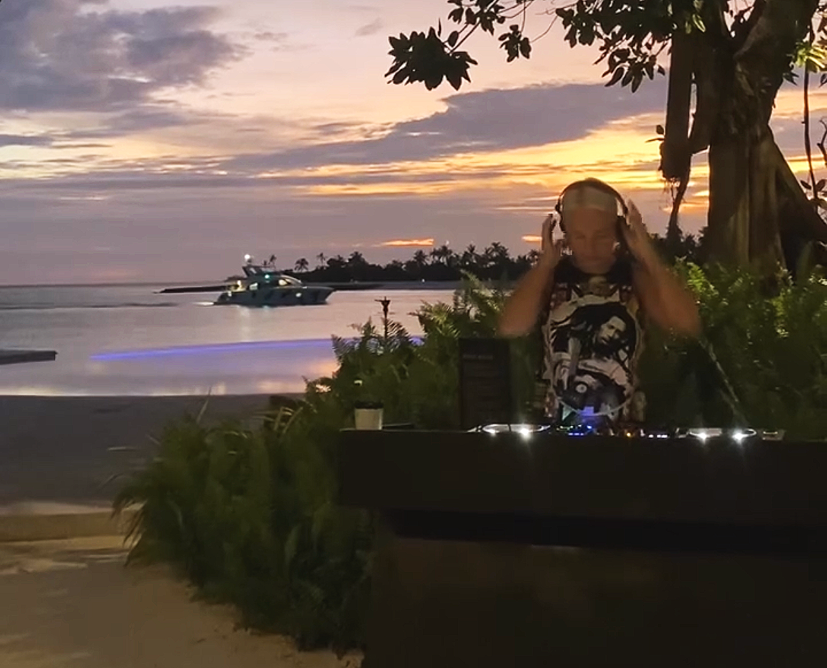 DJ with headphones on at sunset with luxury yacht passing behind