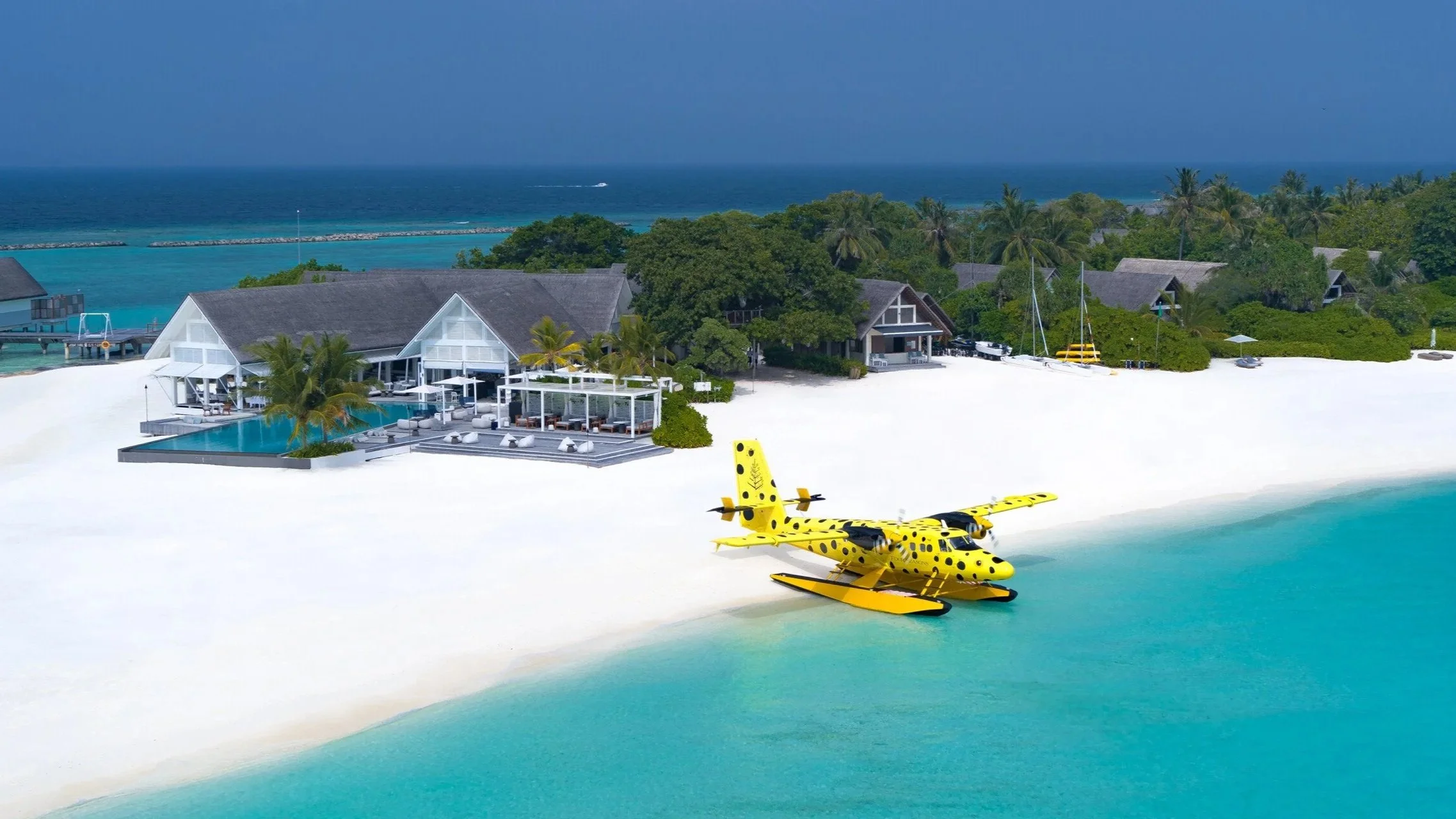 Yellow seaplane with black dots parked on a white sand beach at a resort