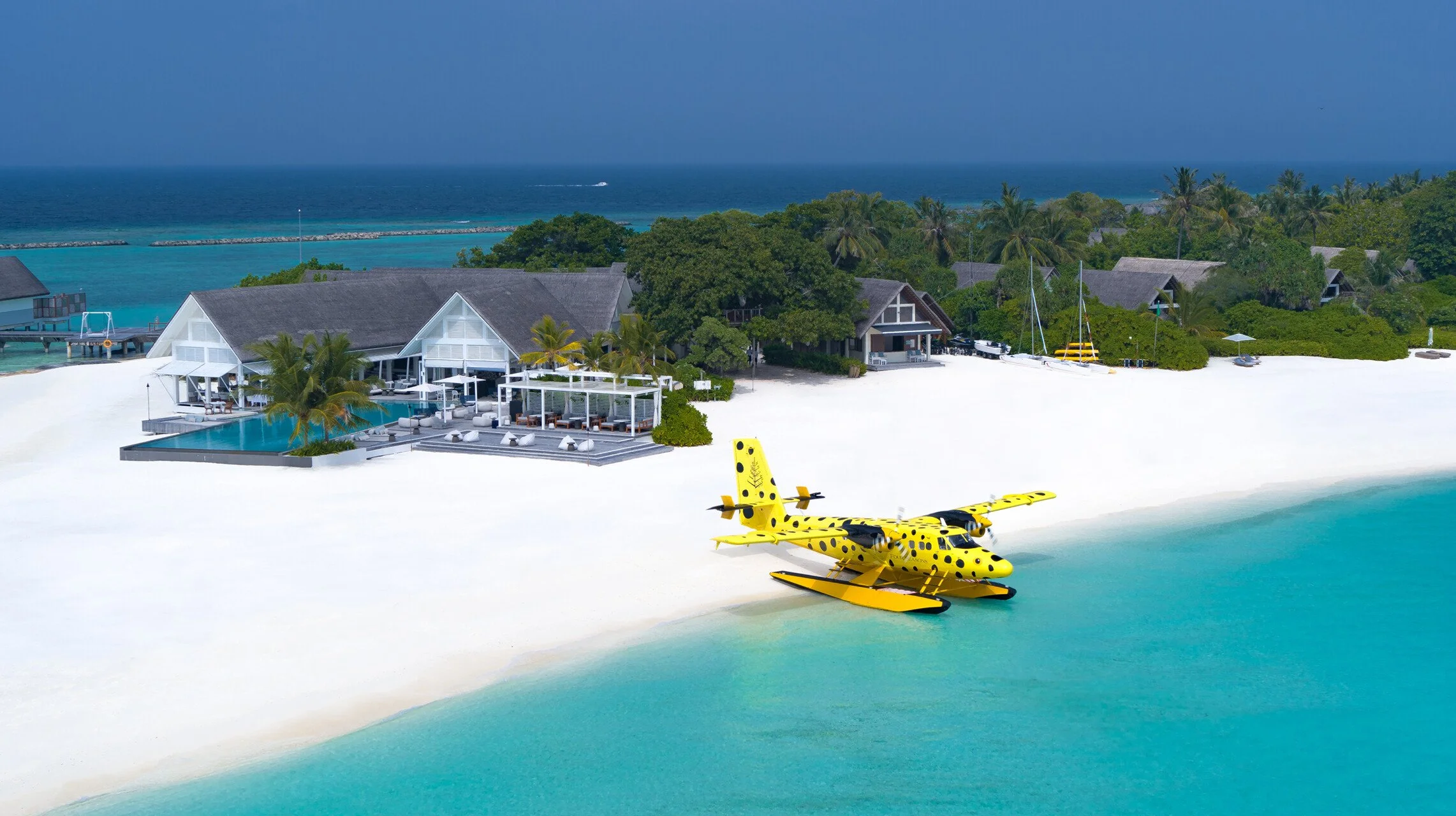 Yellow seaplane with black spots backed onto a beach next to a resort