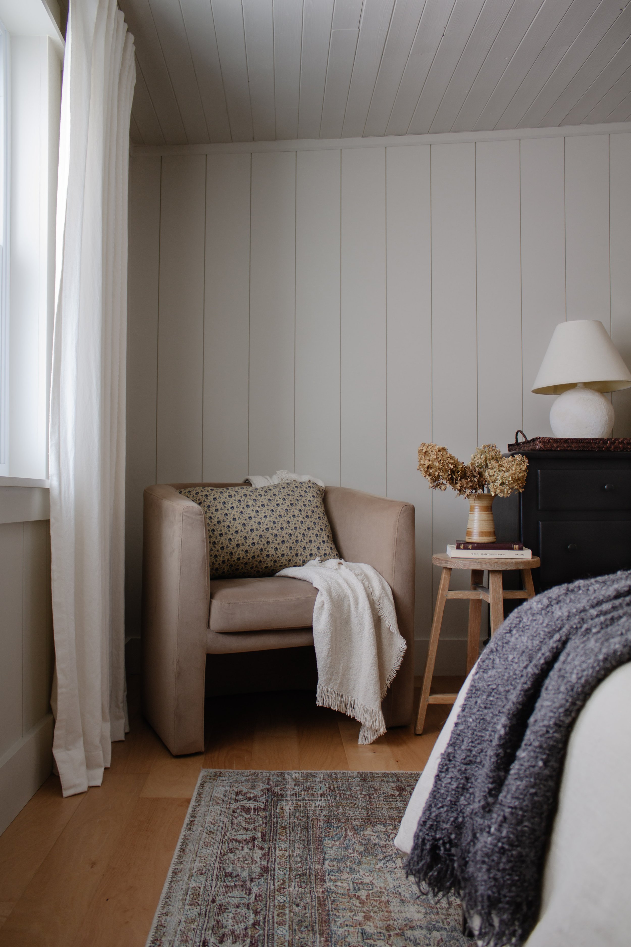 Bedroom styling by Nadine Stay. Vertical plank walls with wood planked ceiling. Putty white paint color. Round barrel chair from Target. Black dresser styling. Dried hydrangea stems. My favorite budget friendly ivory curtains. | Nadine Stay
