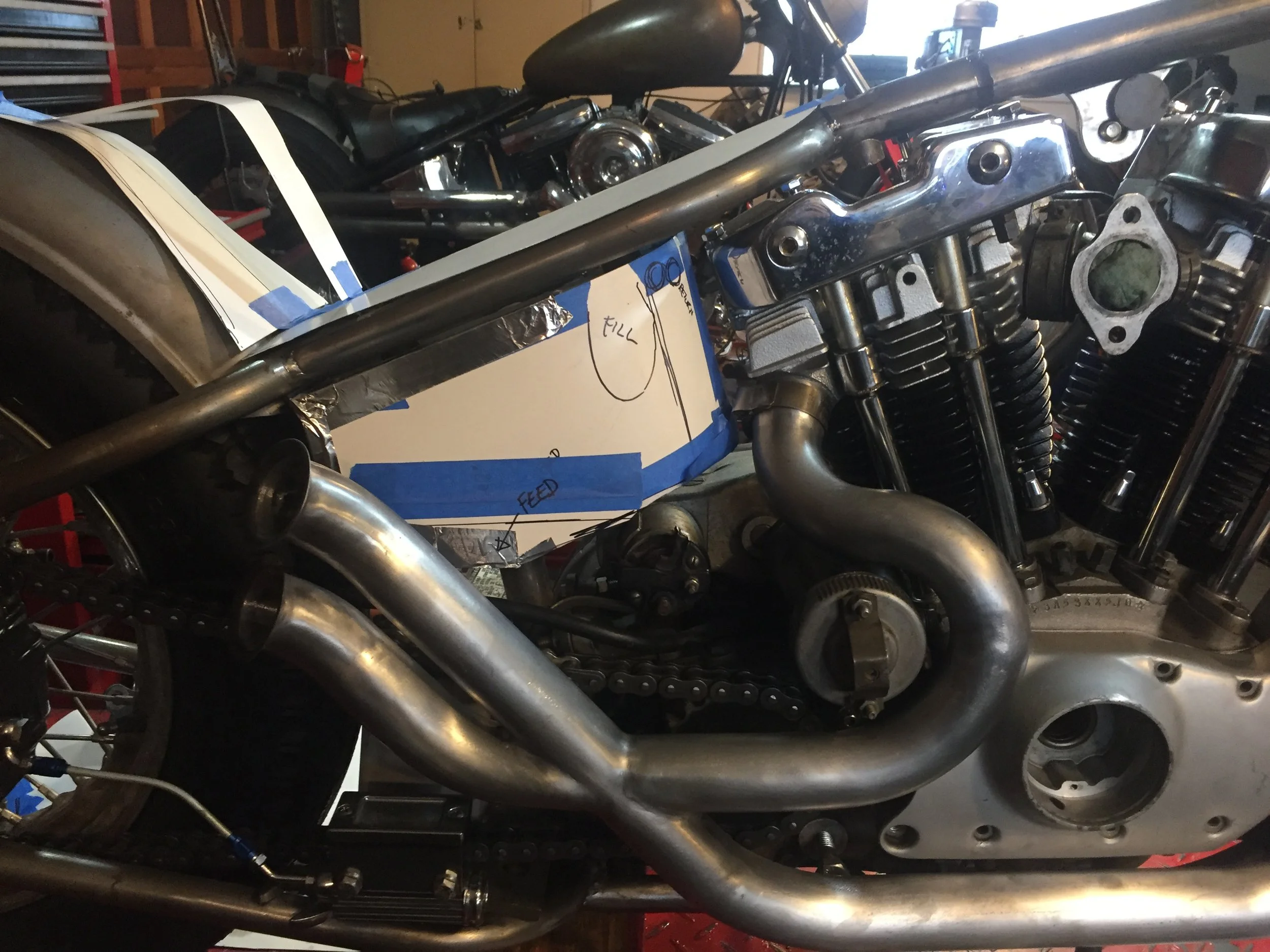  Custom oil tank build for a super skinny Ironhead frame.  This photo shows the mockup/pattern drafting part of the process, where I use cardstock and tape to rough out my design.  You can see there are a number of elements here to work around.  Ther