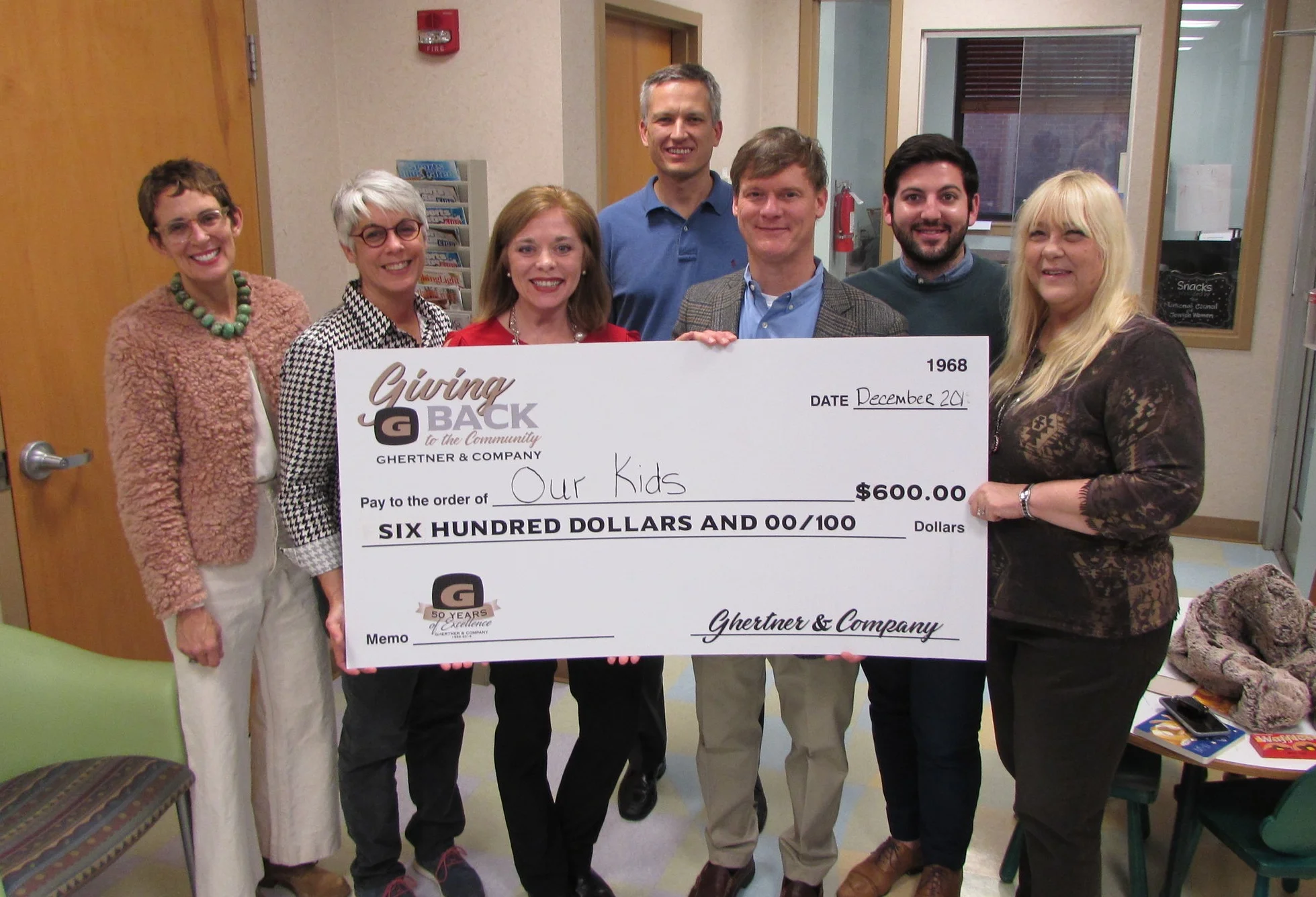Receiving the check on behalf of the Our Kids Center is Hollye Gallion, Denise Alexander, Jill Martindale from Scott Ghertner, Co-President of Ghertner & Company. Others Ghertner & Company associates present are Jaye Kloss, Kerry Chapman and Mark Darden.