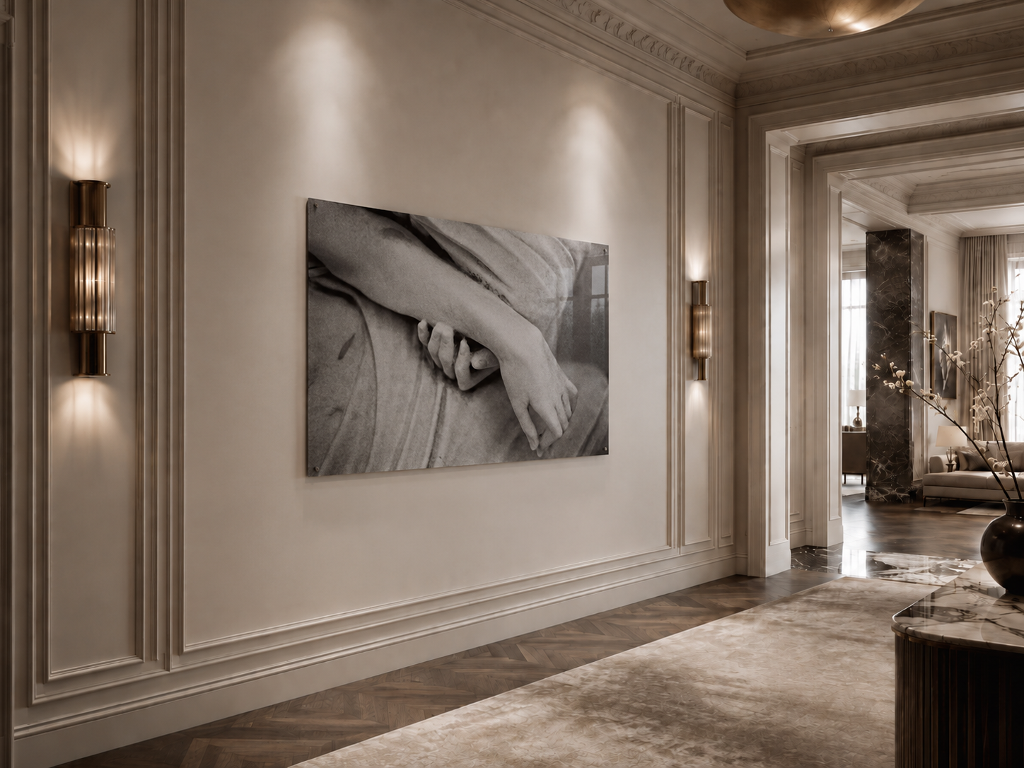 Interior de una sala elegante con paredes claras, iluminación moderna y una obra de arte en blanco y negro que muestra una mano entrelazada con un brazo, decoraciones de madera y un alfombra beige.
