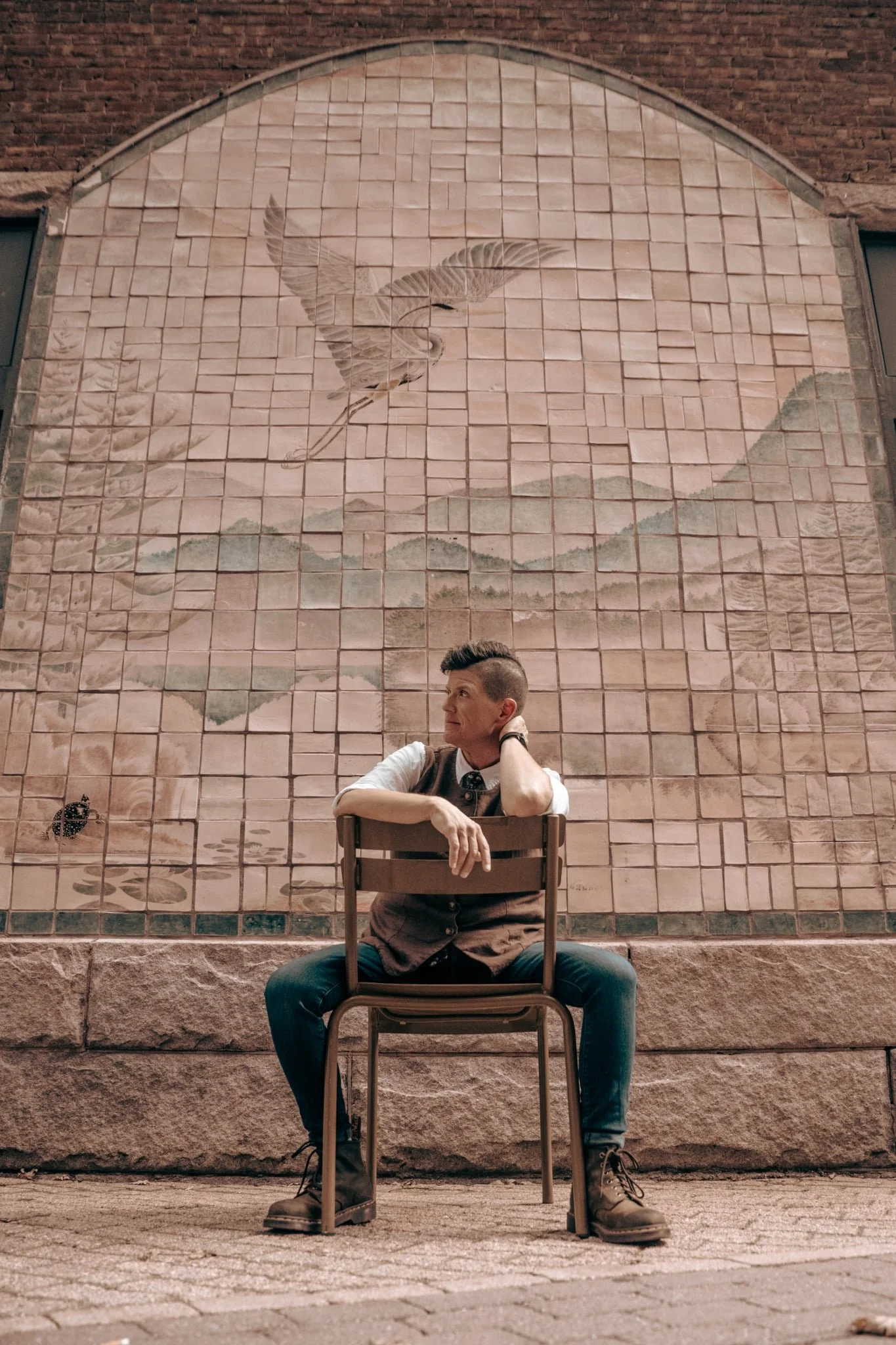 Andrea sitting backwards on chair in front of tile mural outside