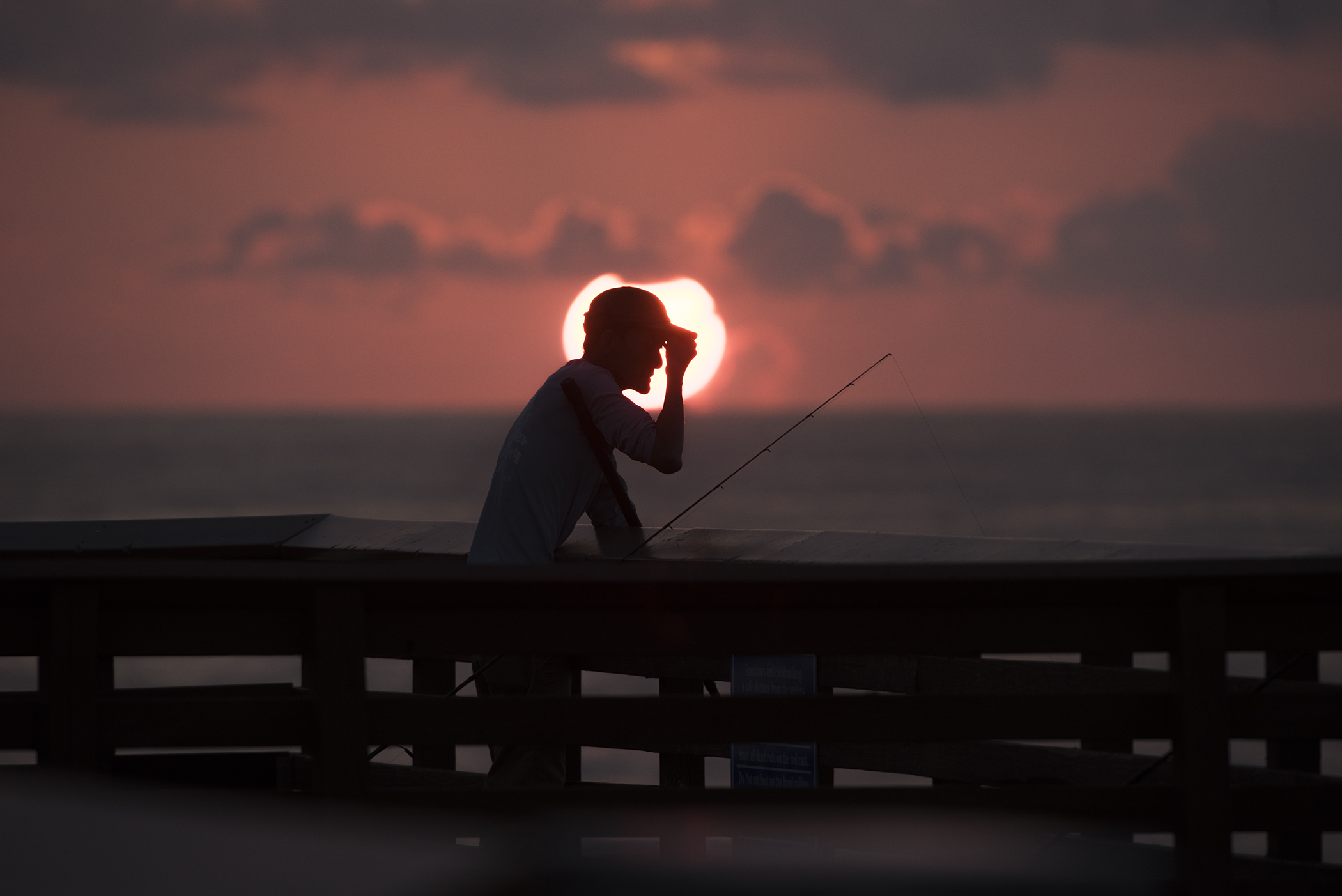  A man who asked not to be identified adjusts his cap while fishing at the Juno Beach Fishing Pier at sunrise. 
