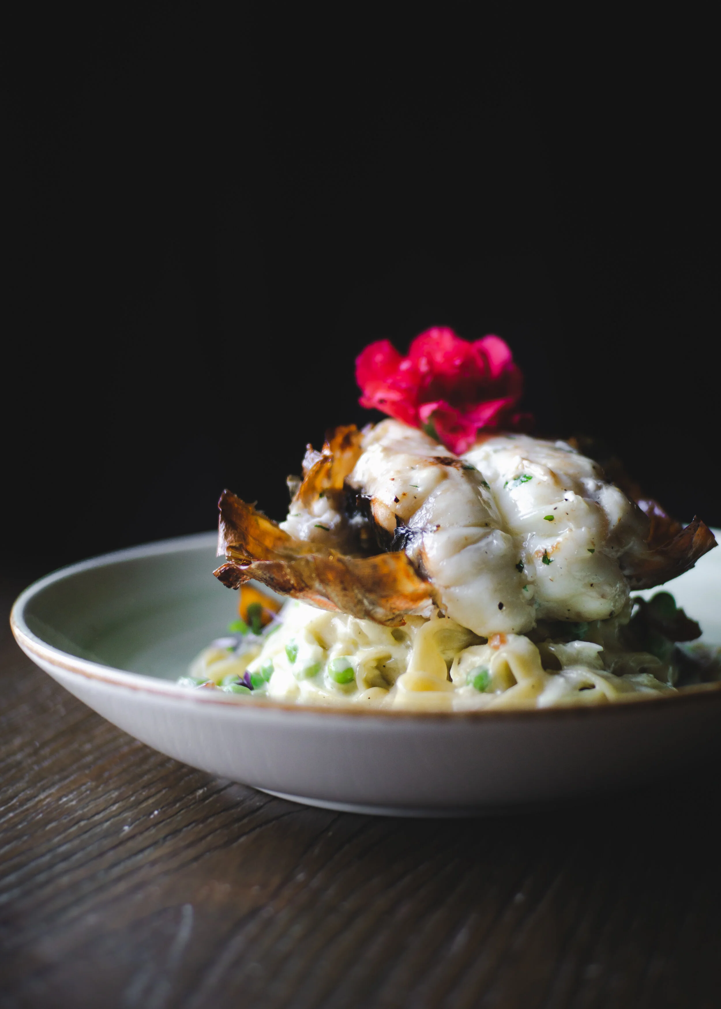 lobster over pasta in white sauce with green peas and a flower (Copy)