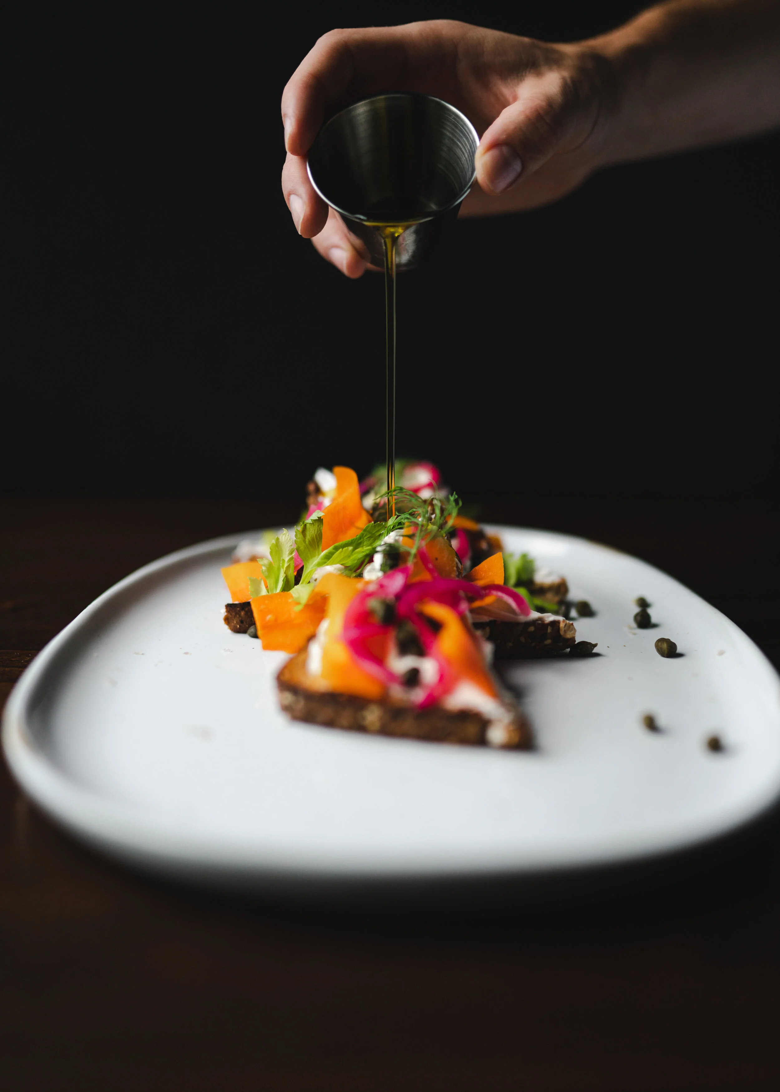 hand pouring syrup on vegan lox with carrots and capers (Copy)