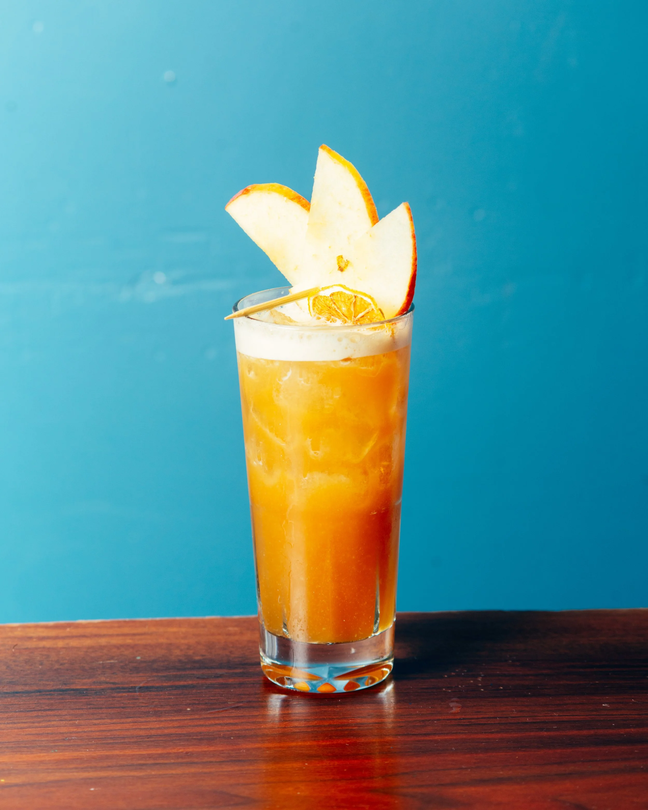 orange cocktail with apple garnish against blue wall (Copy)