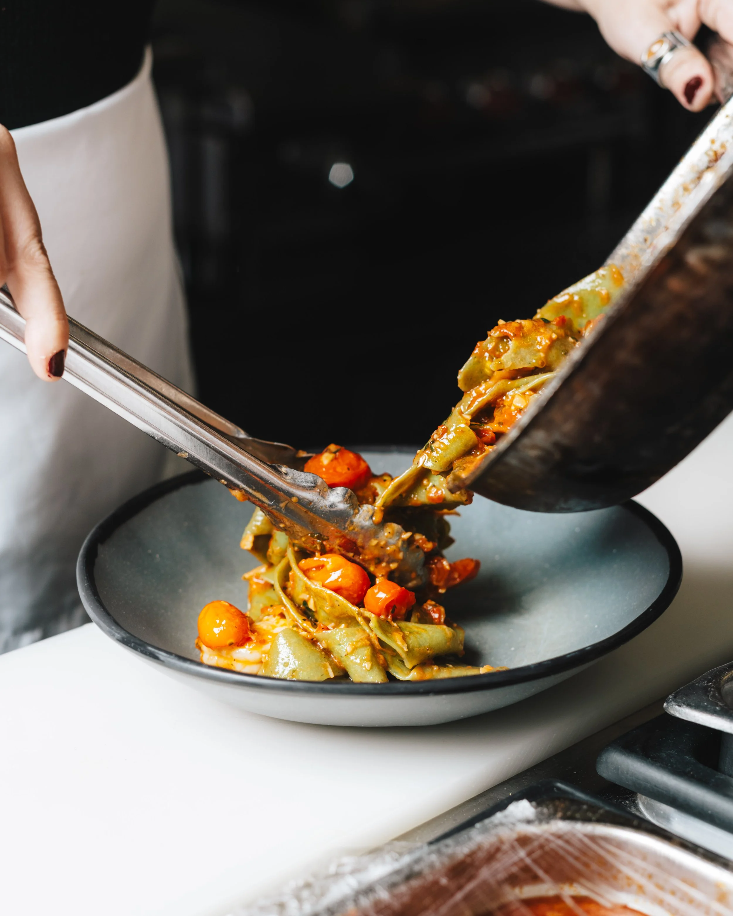 using tongs to plate shrimp pappardelle into a ceramic bowl (Copy)