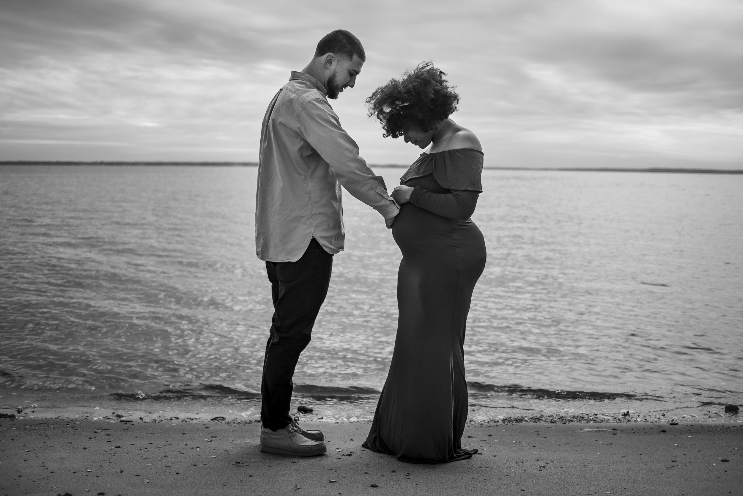 Black and white image of pregnant couple on the beach.