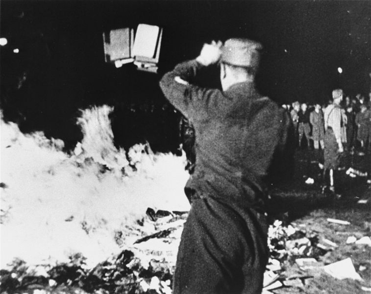 A group of Nazis throw documents and books into a fire in the street.