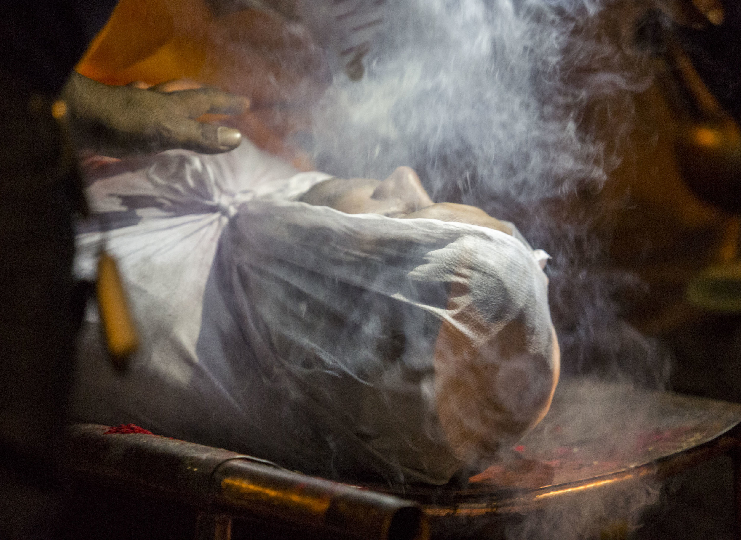  The face of a deceased person is illuminated by flashlight at a night ceremony on May 23, 2016, in Kathmandu, Nepal. Incense smoke is used to guide the spirit out and as an offering to the deities. 