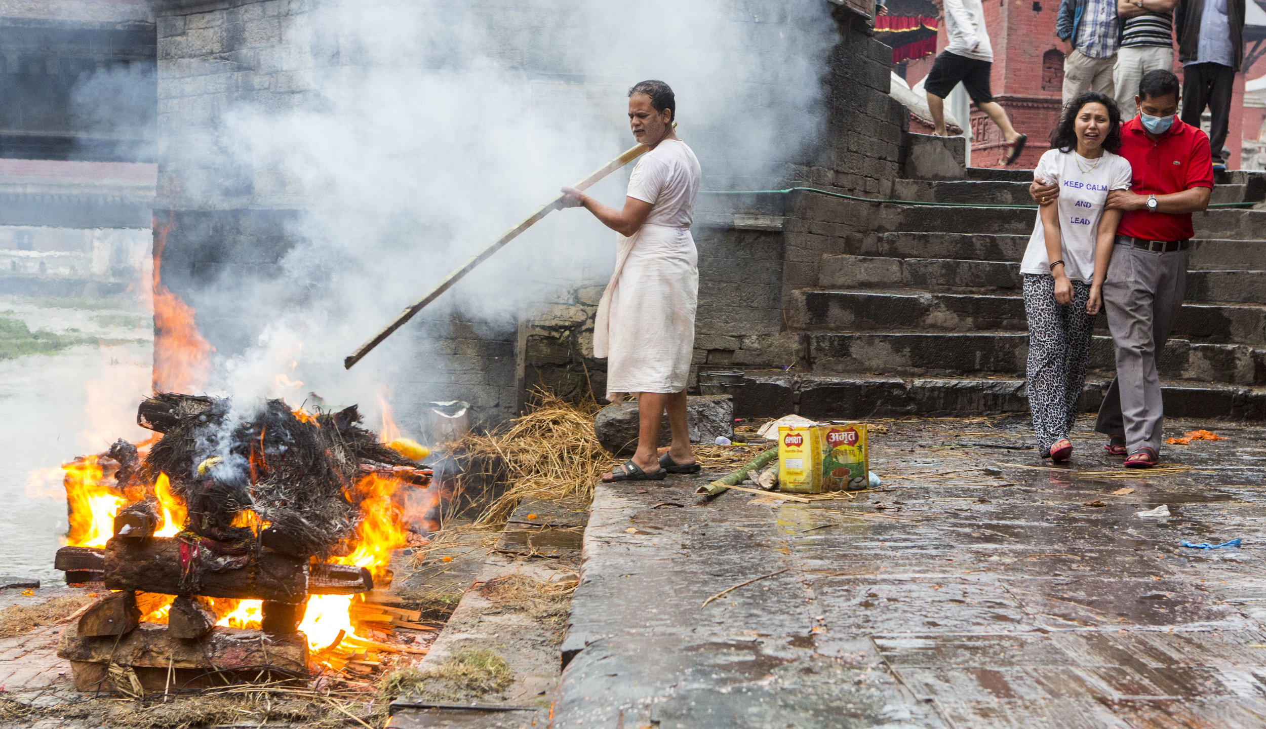  An undertaker cremates a body as family members pass by on May 24, 2016, at Pashupati in Kathmandu, Nepal. 