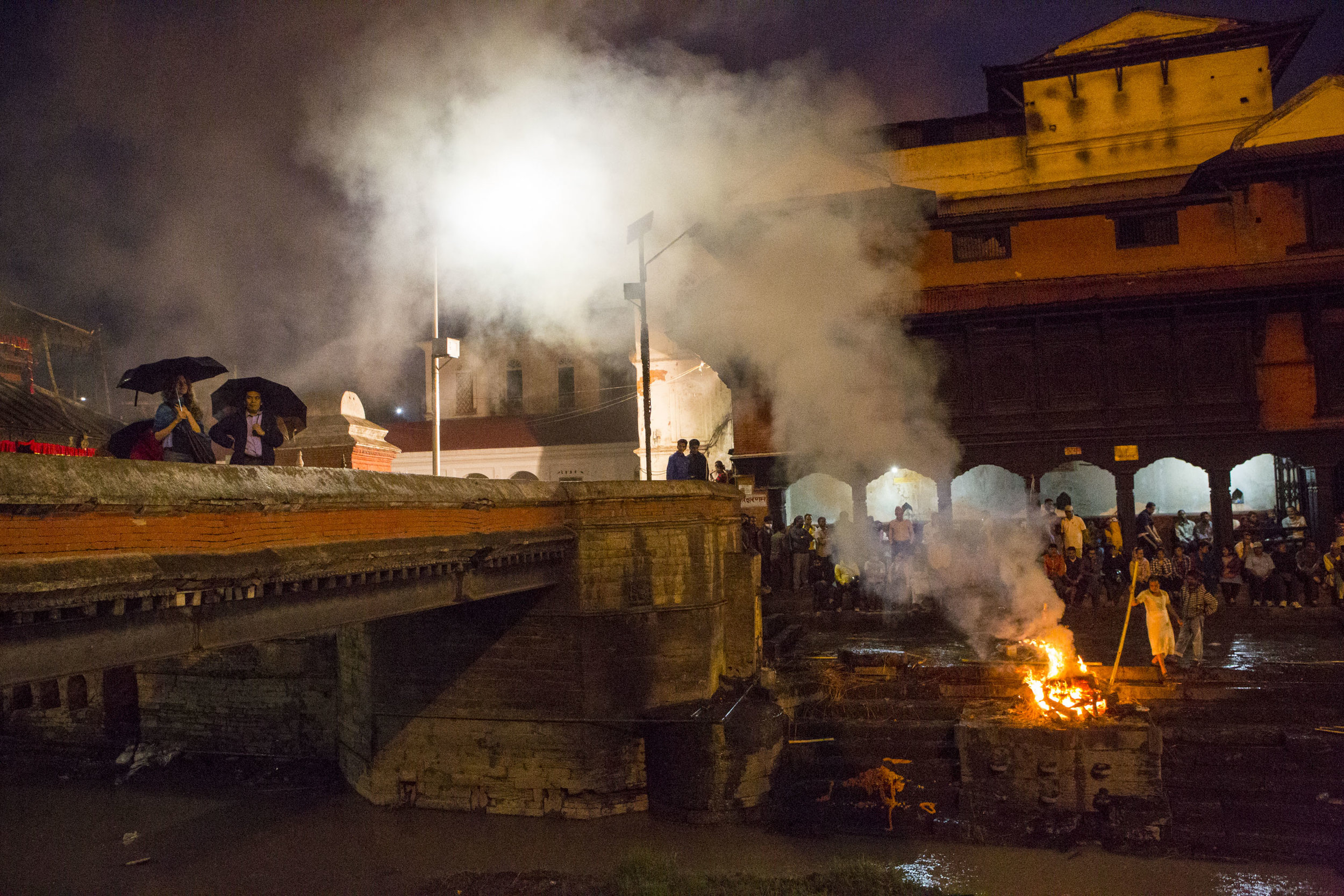  Smoke billows from the ghat where the traditional cremations are performed. Cremations continue through the night until the ashes are released into the Bagmati River where the spirit will flow into reincarnation. 