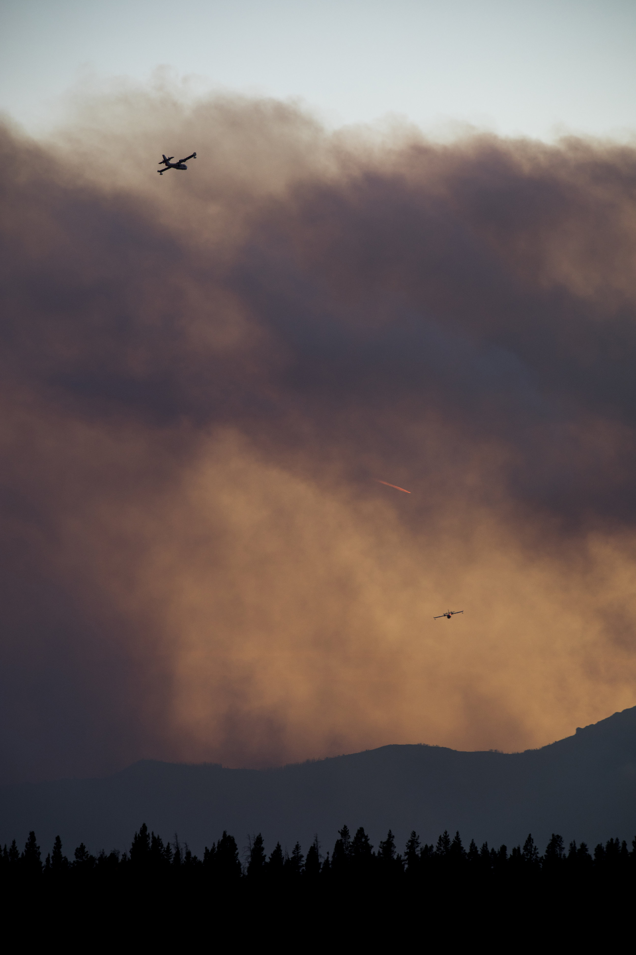  Aerial support flies toward the Roosevelt Fire during wildfire suppression efforts Thursday night. Planes and helicopters have been dropping water and fire retardant in an attempt to save homes in the Bondurant area. 