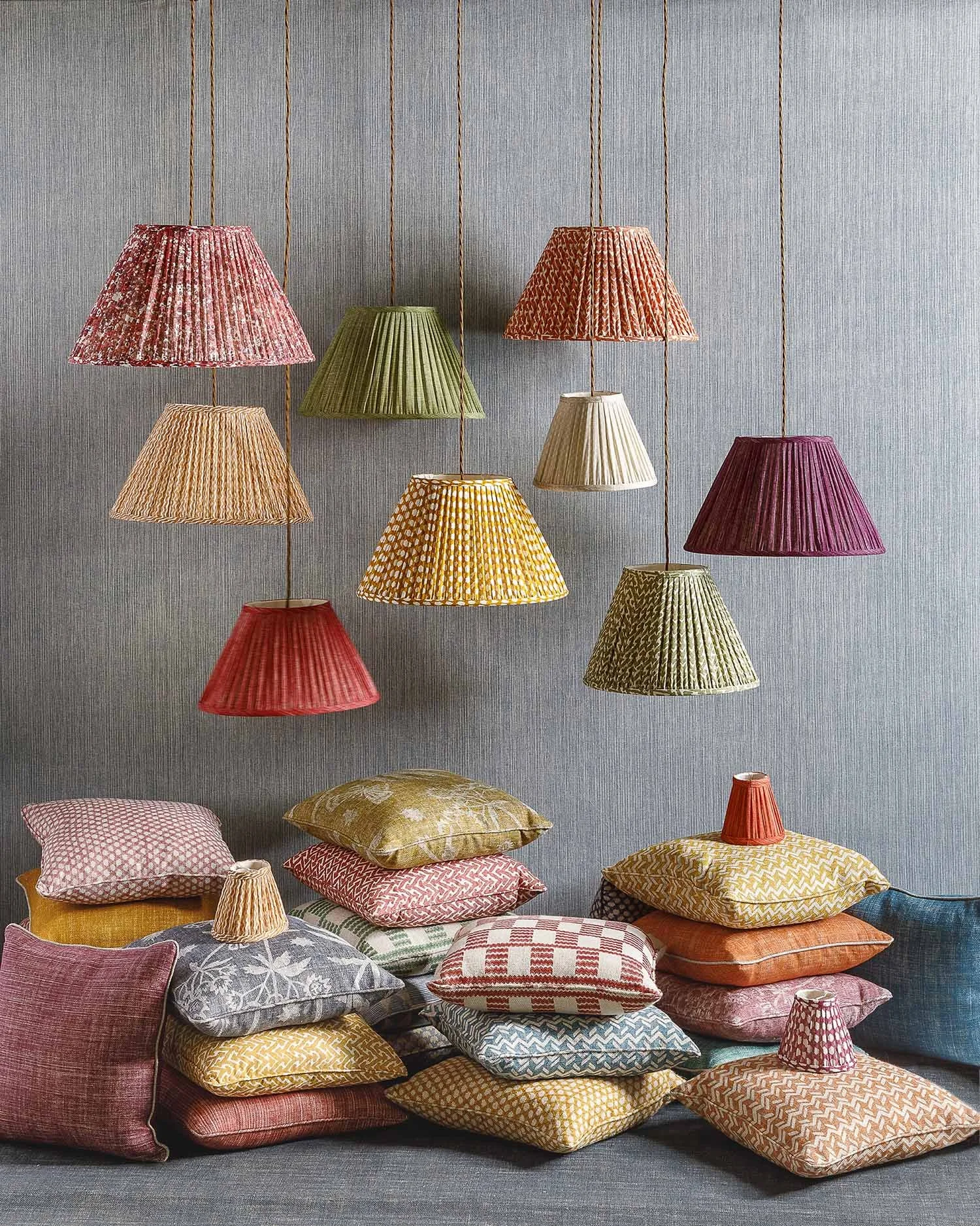 Several colorful hanging lamps above a pile of various patterned pillows on a grey surface.