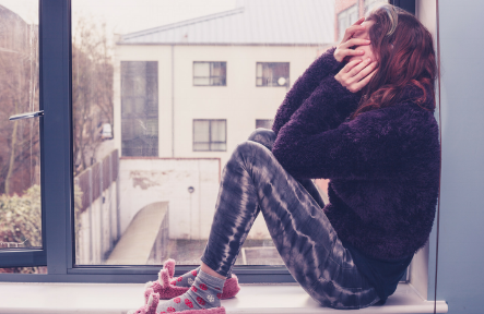 A woman sits in a window covering her face.
