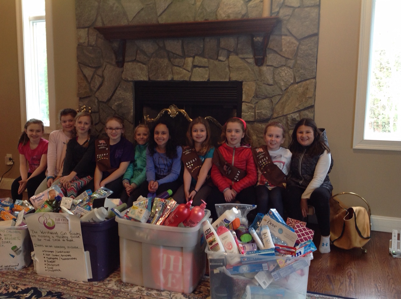 A Girl Scout troop sits with large bins of toiletry donations for Circle of Hope.