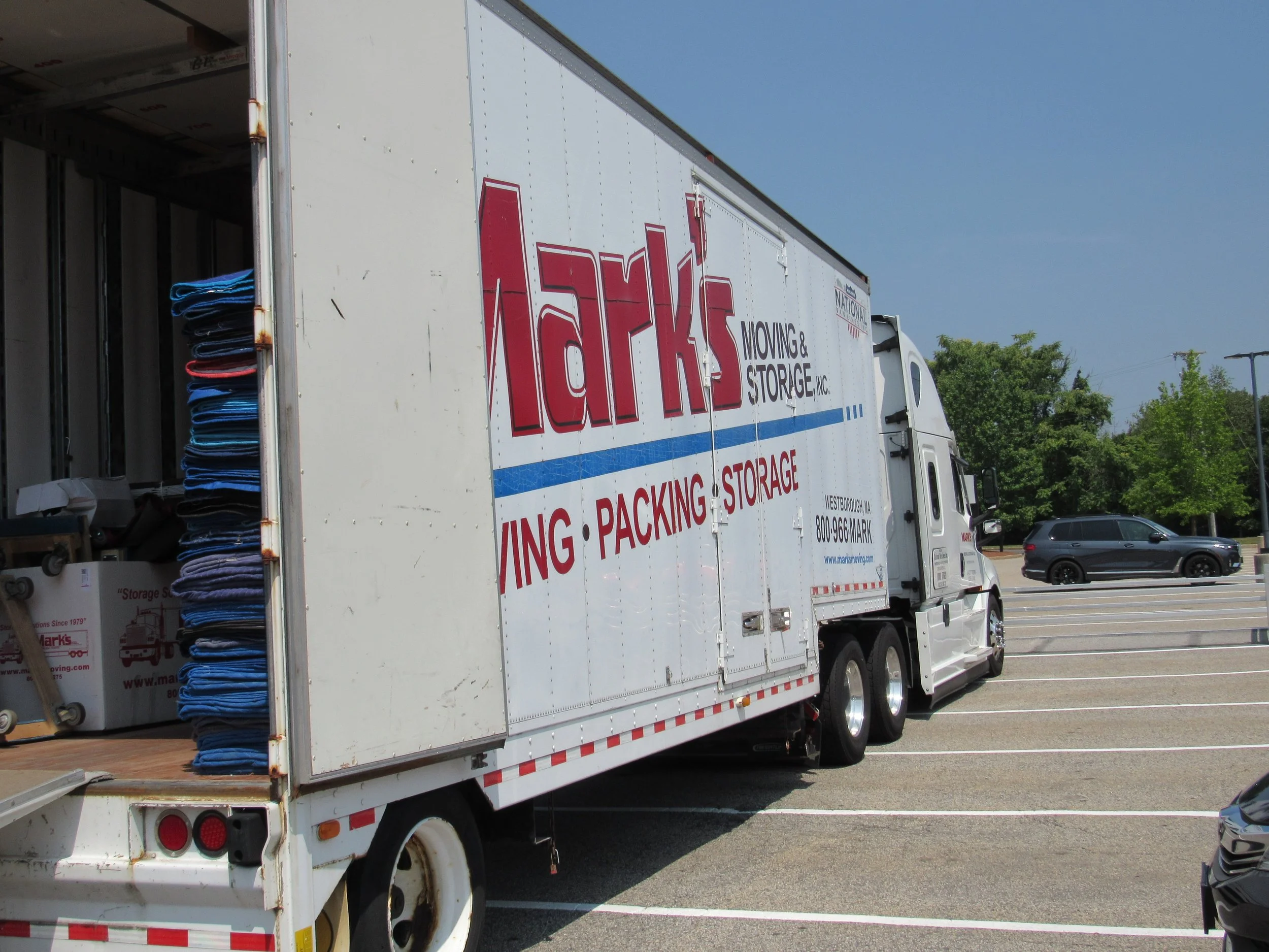 A Mark's Moving truck is parked in a parking lot on a bright, sunny day.