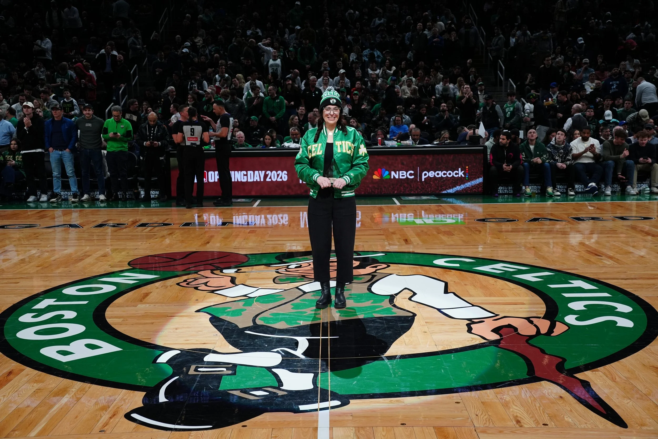Ari Barbanell standing on the parquet floor at TD Garden wearing a green Celtics jacket and beanie.
