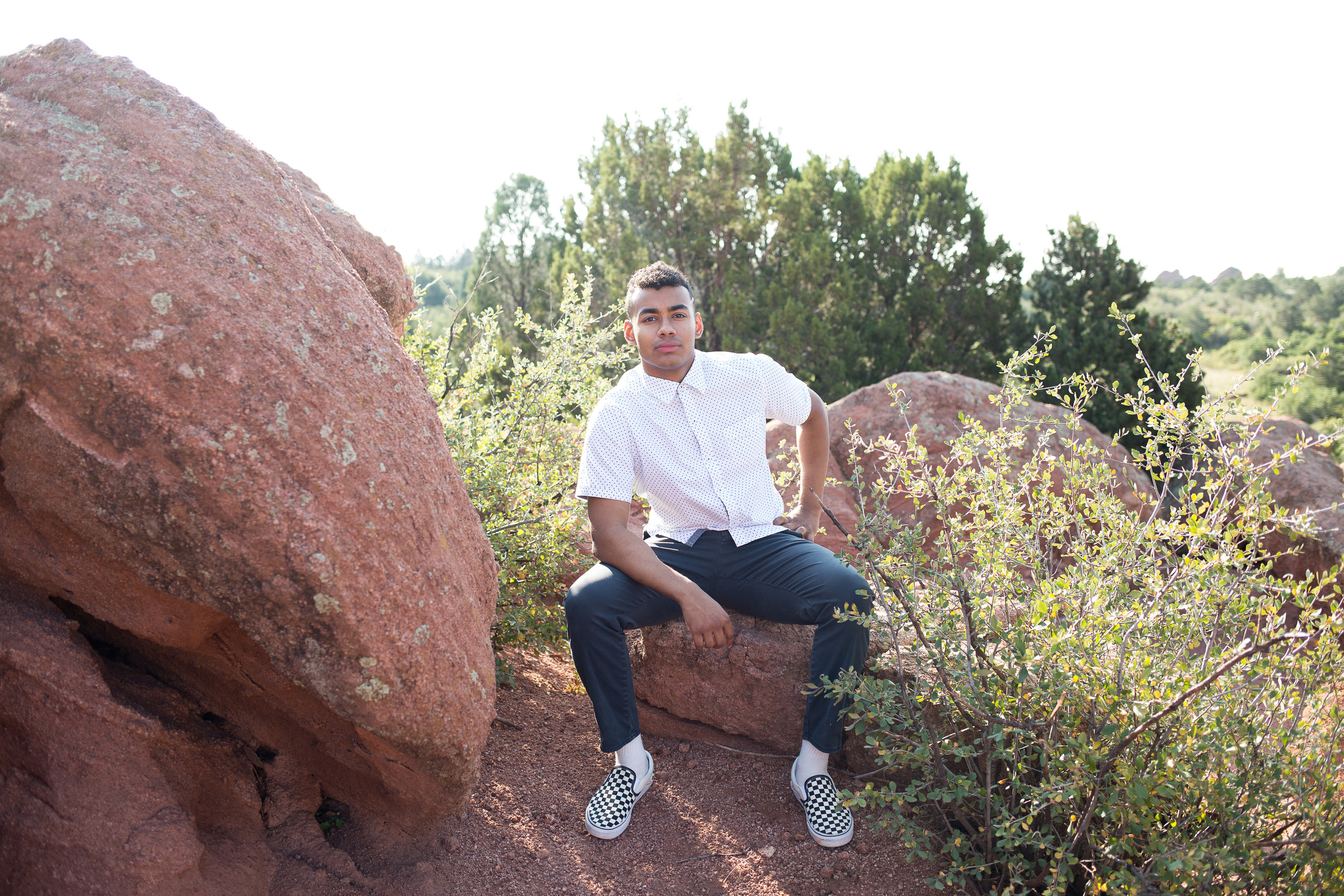 Stacy Carosa Photography senior boy sitting on red rock in Garden of the Gods by green bushes