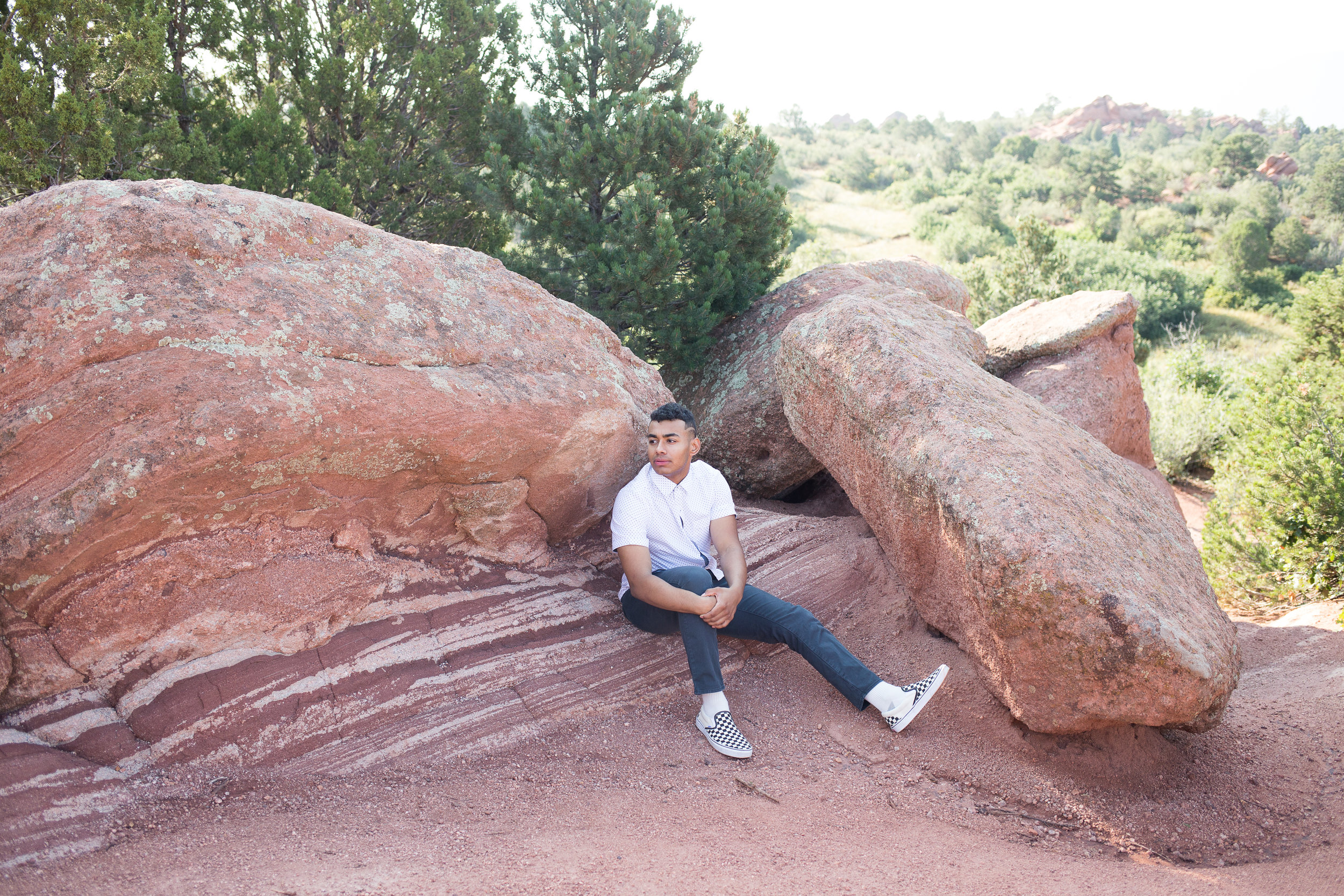 Senior boy looking in the distance while sitting on red rocks in Garden of the Gods for senior photos, Stacy Carosa Photography