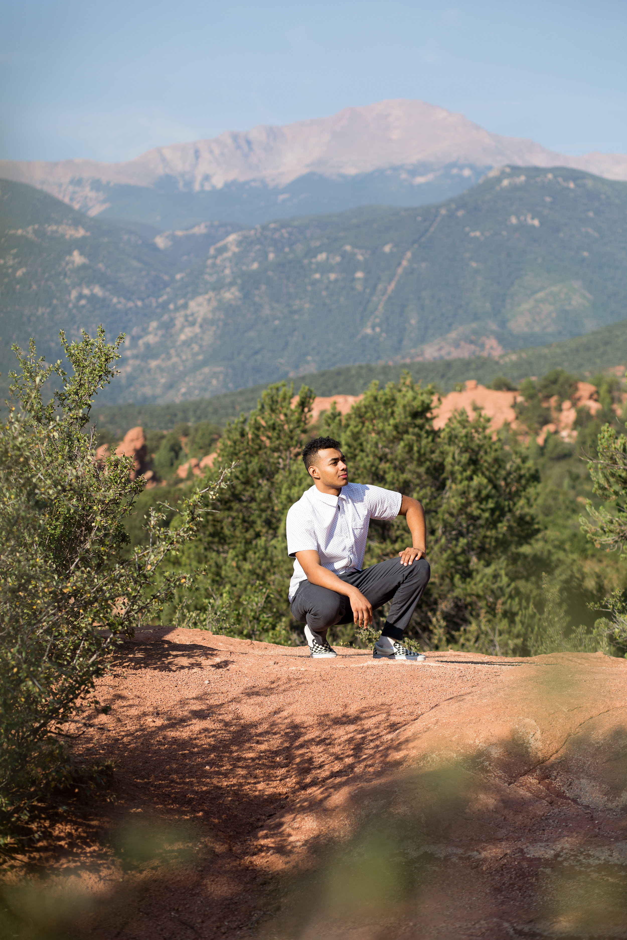 Liberty High School senior kneeling on rocks in front of Pikes Peak in Garden of the Gods looking in the distance Stacy Carosa Photography