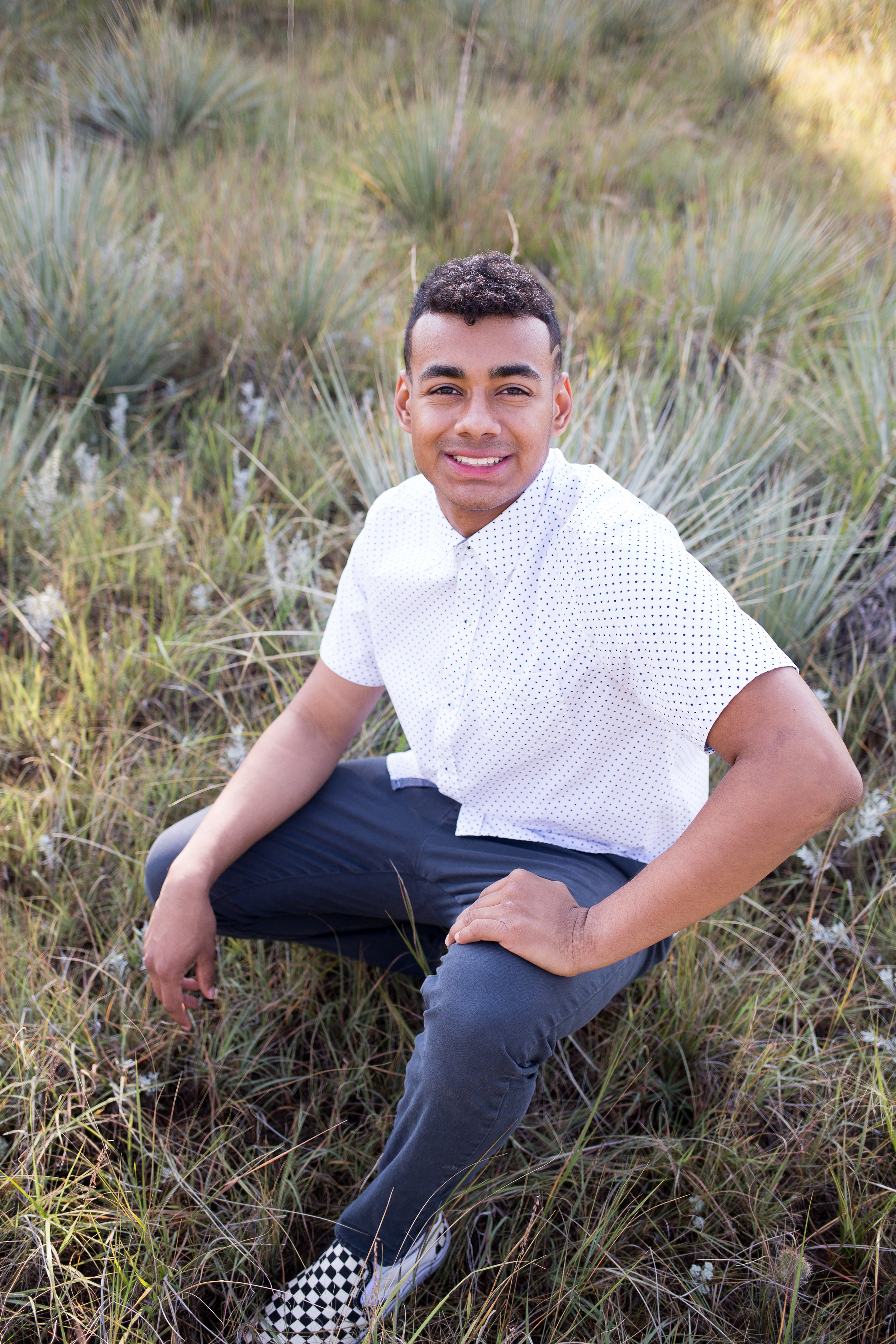 Liberty High School Senior boy sitting in tall grasses in Garden of the Gods for senior photos while smiling at camera Stacy Carosa Photography