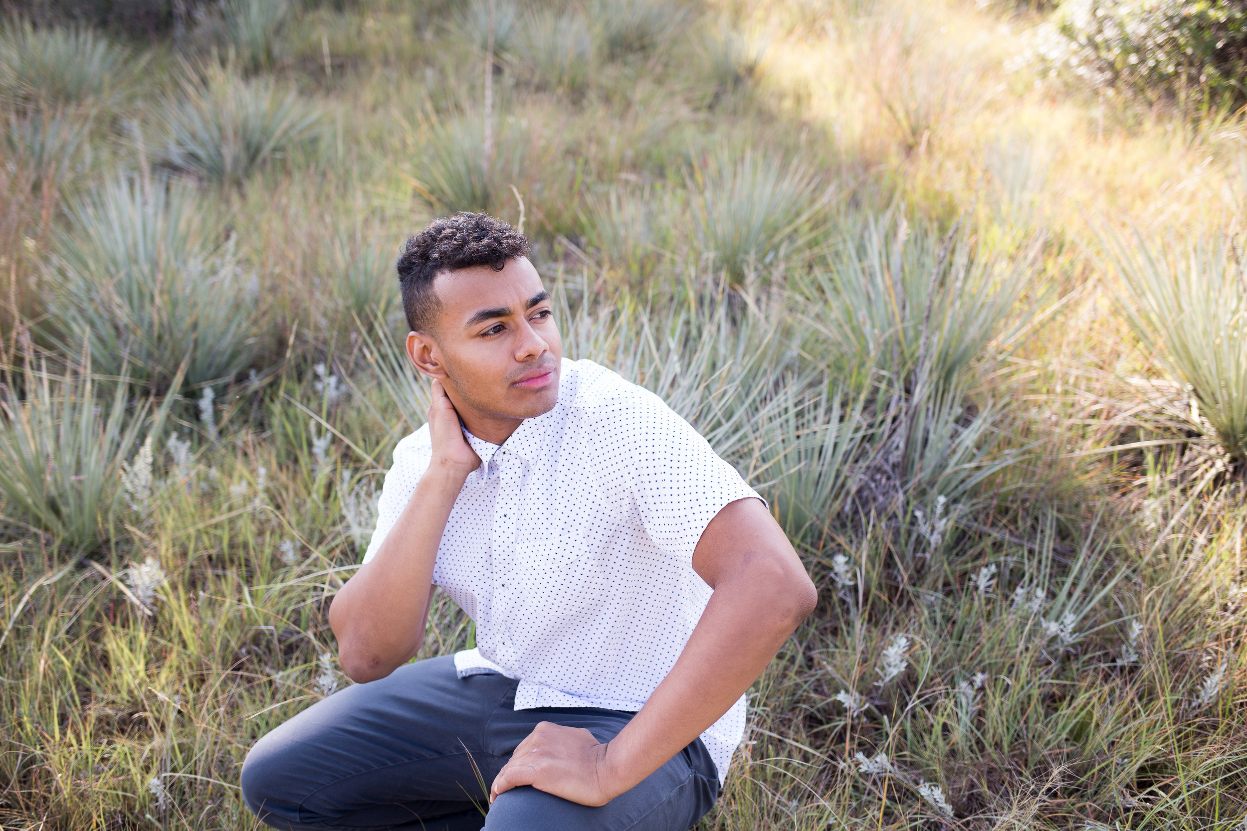 Senior boy sitting in the tall grasses in Garden of the Gods park looking in the distance Stacy Carosa Photography Liberty High School Colorado Springs senior photos