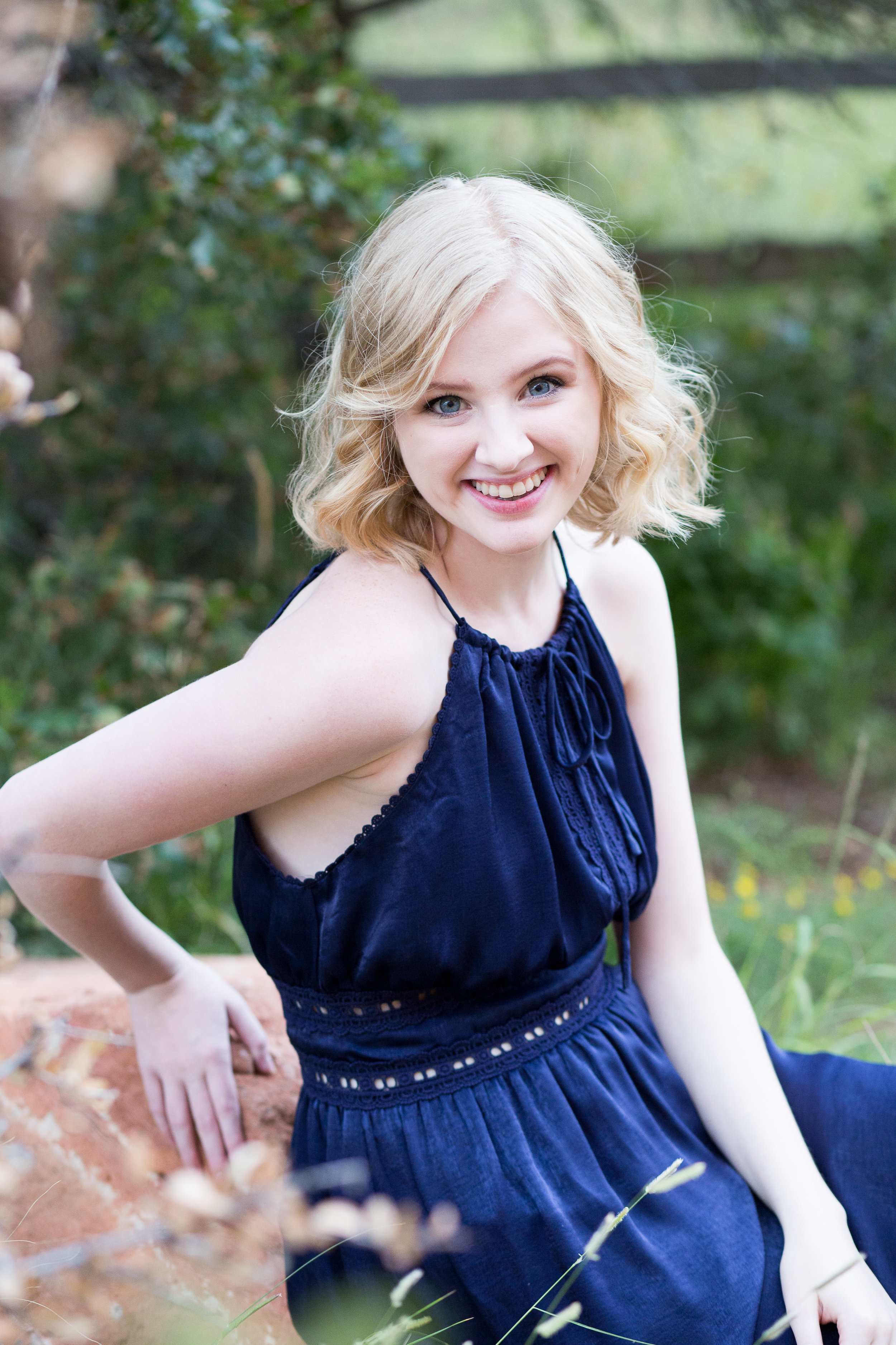 Senior photo session at Garden of the Gods with girl sitting on rock leaning toward the camera smiling, Stacy Carosa Photography, Colorado Springs