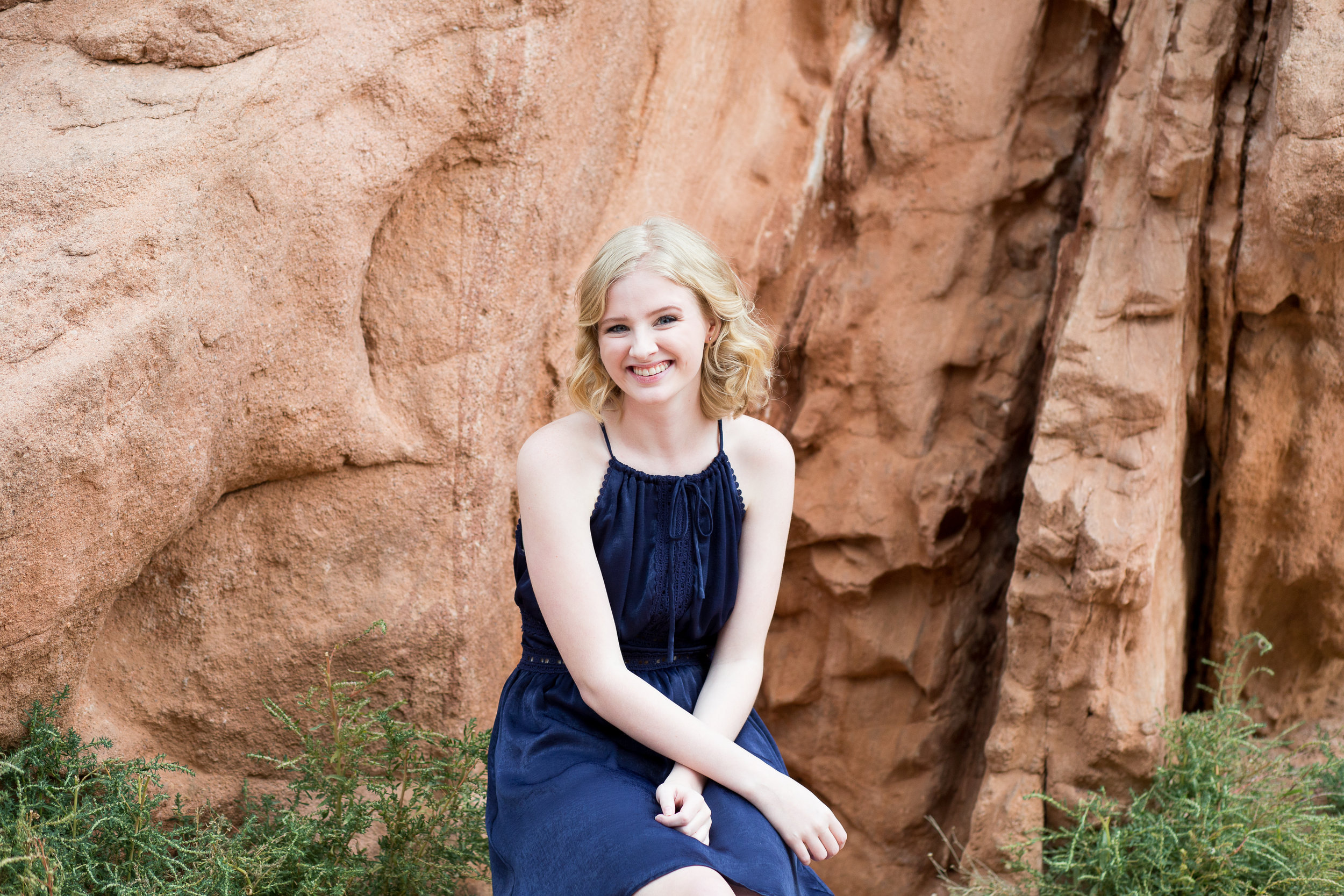 In Garden of the Gods for a senior session, girl sitting in front of red rock with arms crossed smiling, Stacy Carosa Photograpy, Colorado Springs