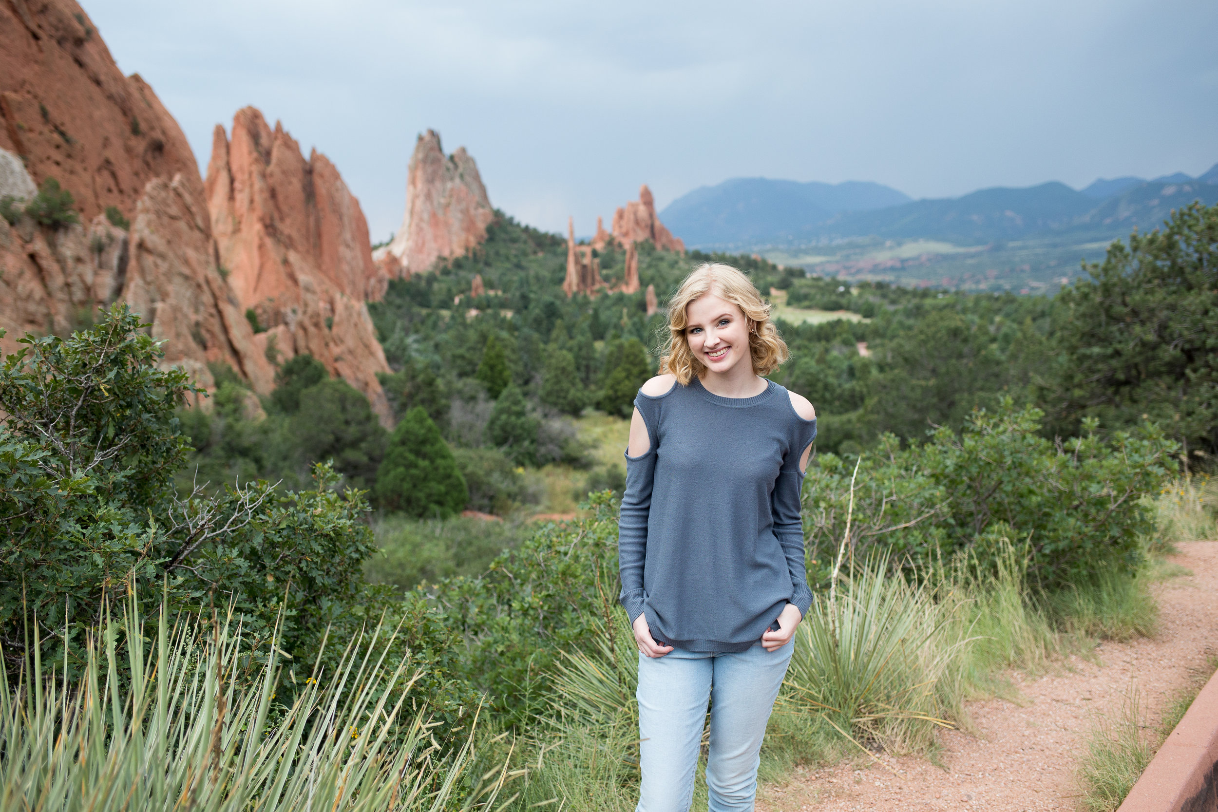 Beautiful Garden of the Gods backdrop for a senior session, girl with hands in pockets and green bushes around, Stacy Carosa Photography, Colorado Springs