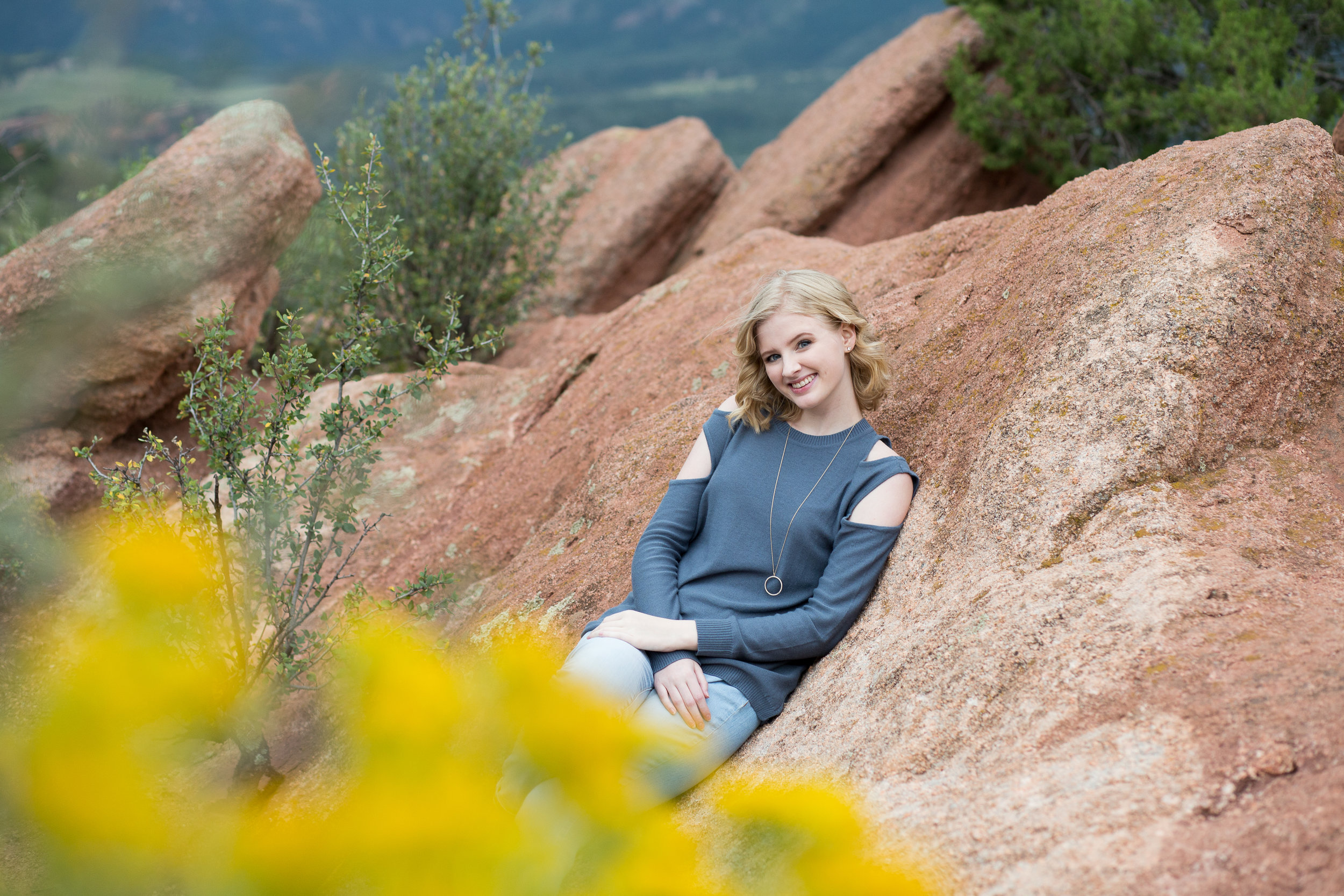 Yellow flowers in the foreground and senior girl leaning against red rock in Garden of the Gods park, Stacy Carosa Photography, Colorado Springs