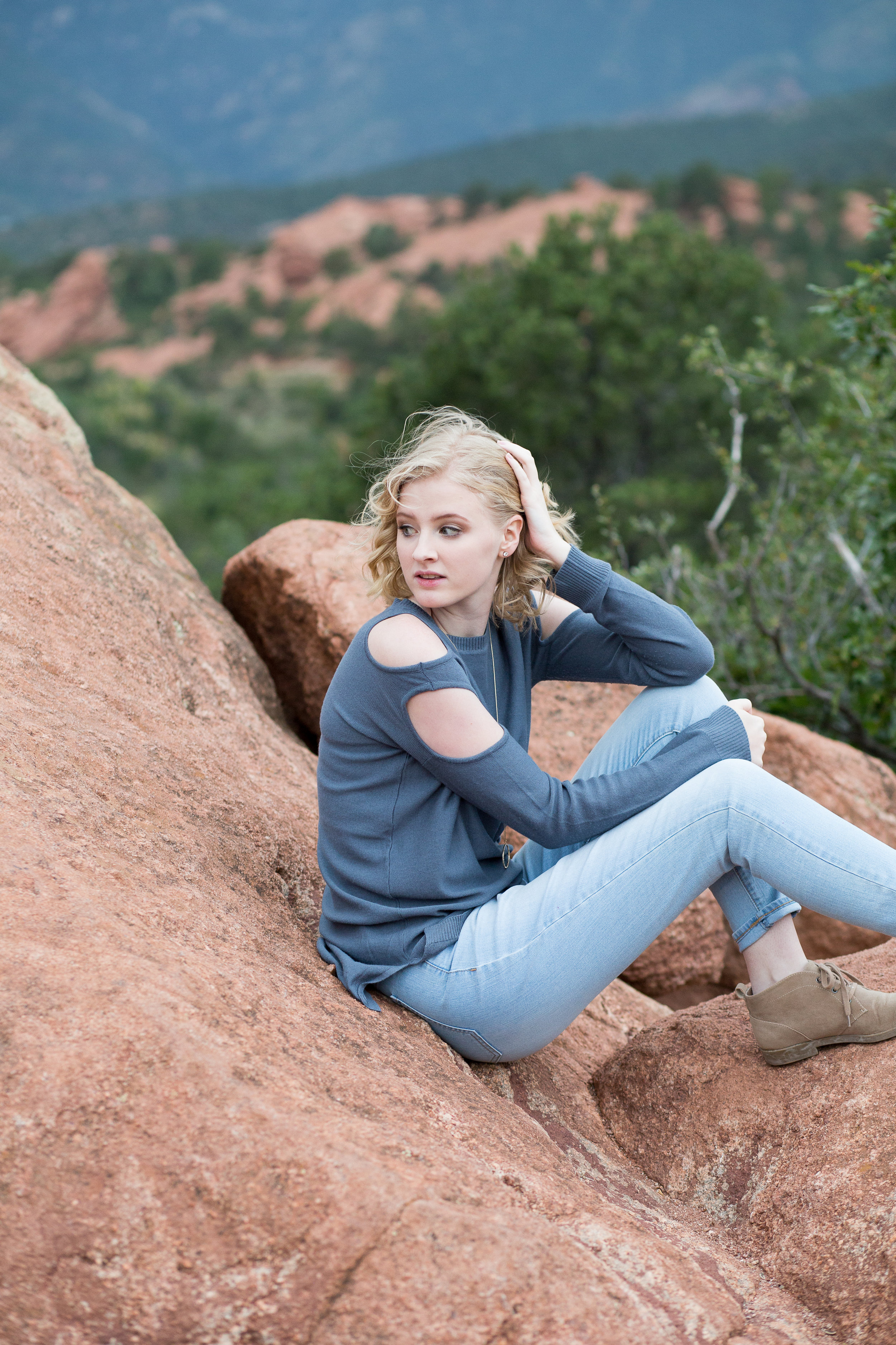 Girl sitting on red rock in Garden of the God with hand in hair and looking behind her, Colorado Springs, Stacy Carosa Photography Senior Session