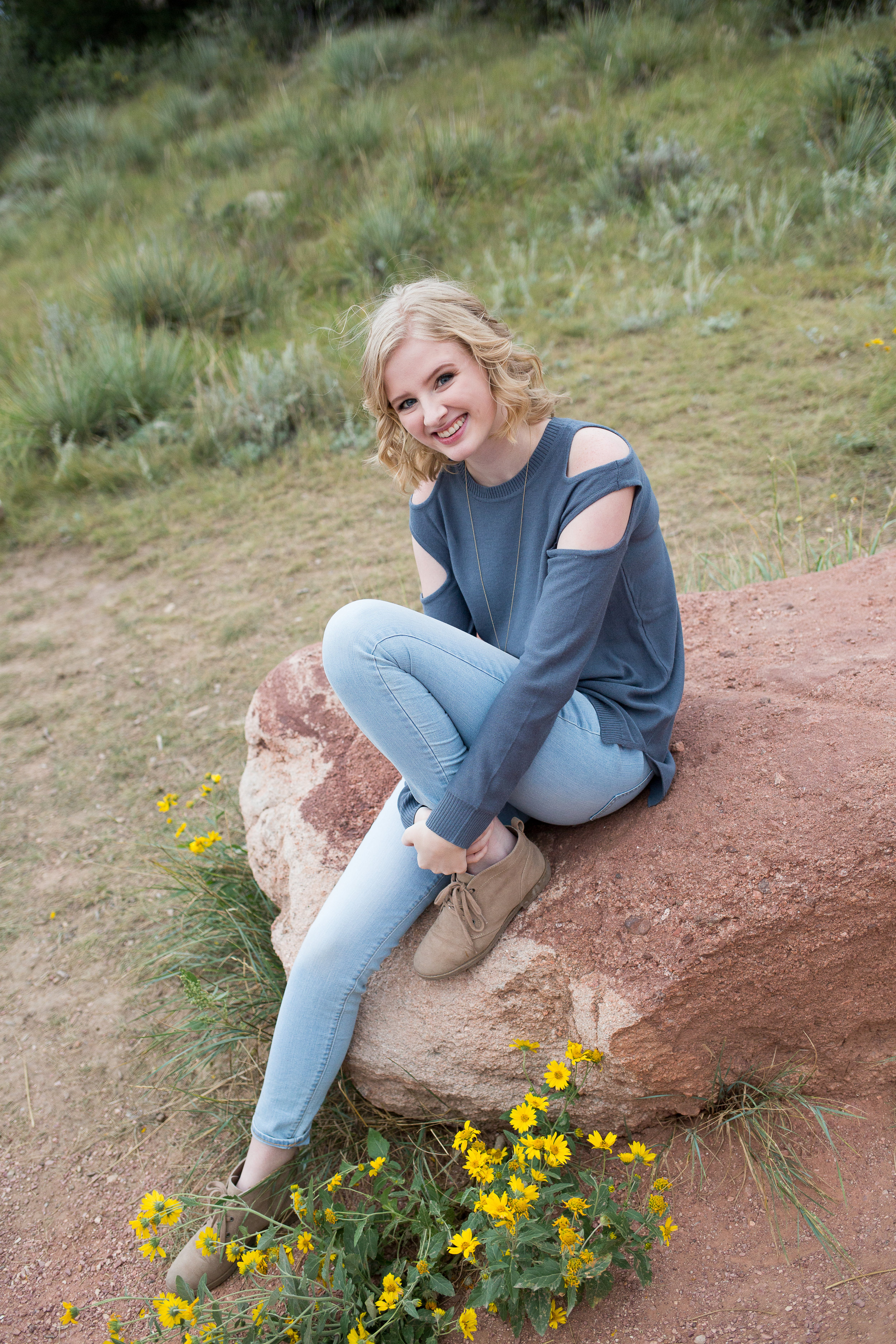 Blond girl sitting on rock and hugging her knee in Garden of the Gods park for her senior photos in Colorado Springs, Stacy Carosa Photography, High School Seniors