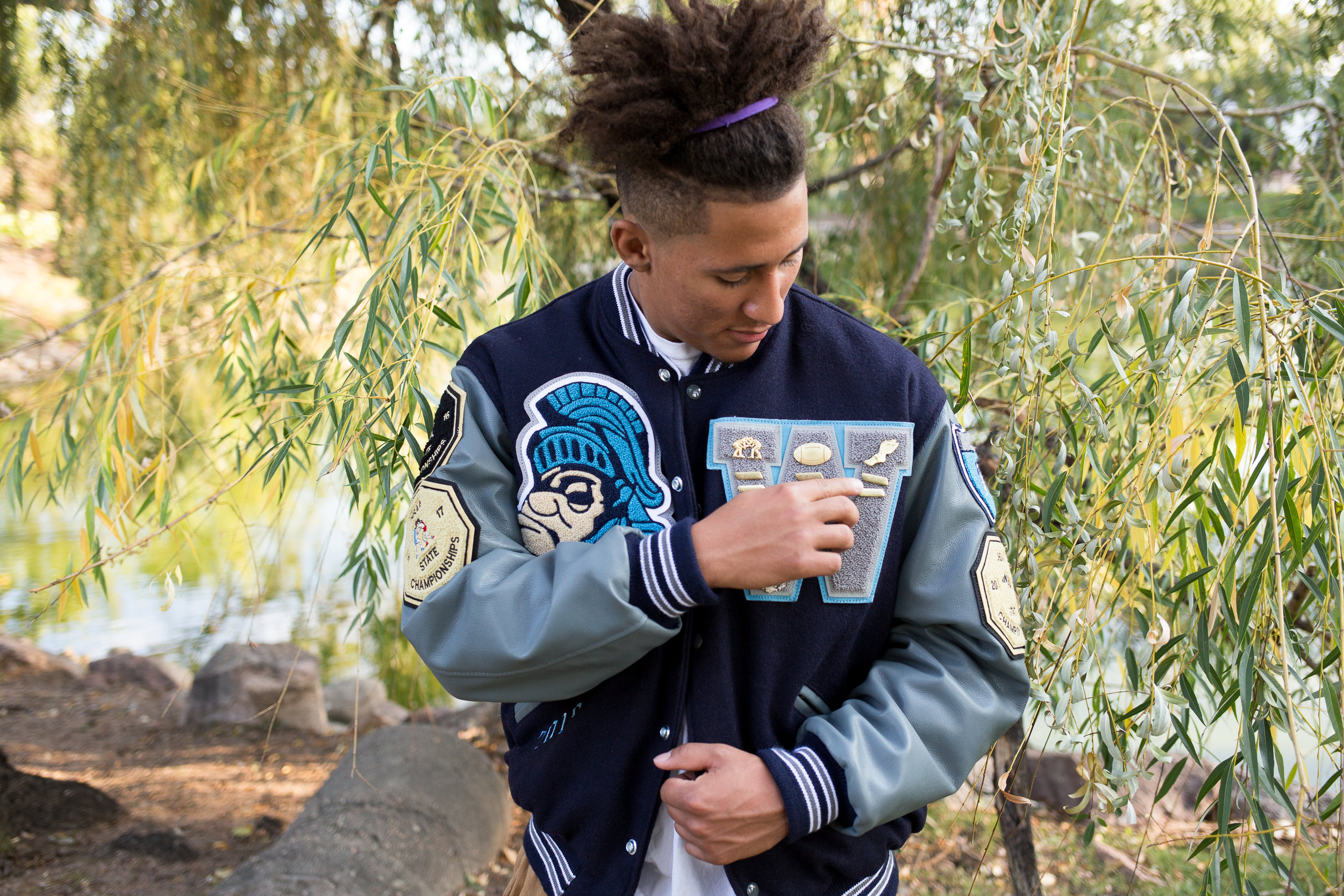 Colorado Springs Senior Photography Widefield High School senior adjusting the pins on his varsity jacket in front of a willow tree Stacy Carosa Photography 
