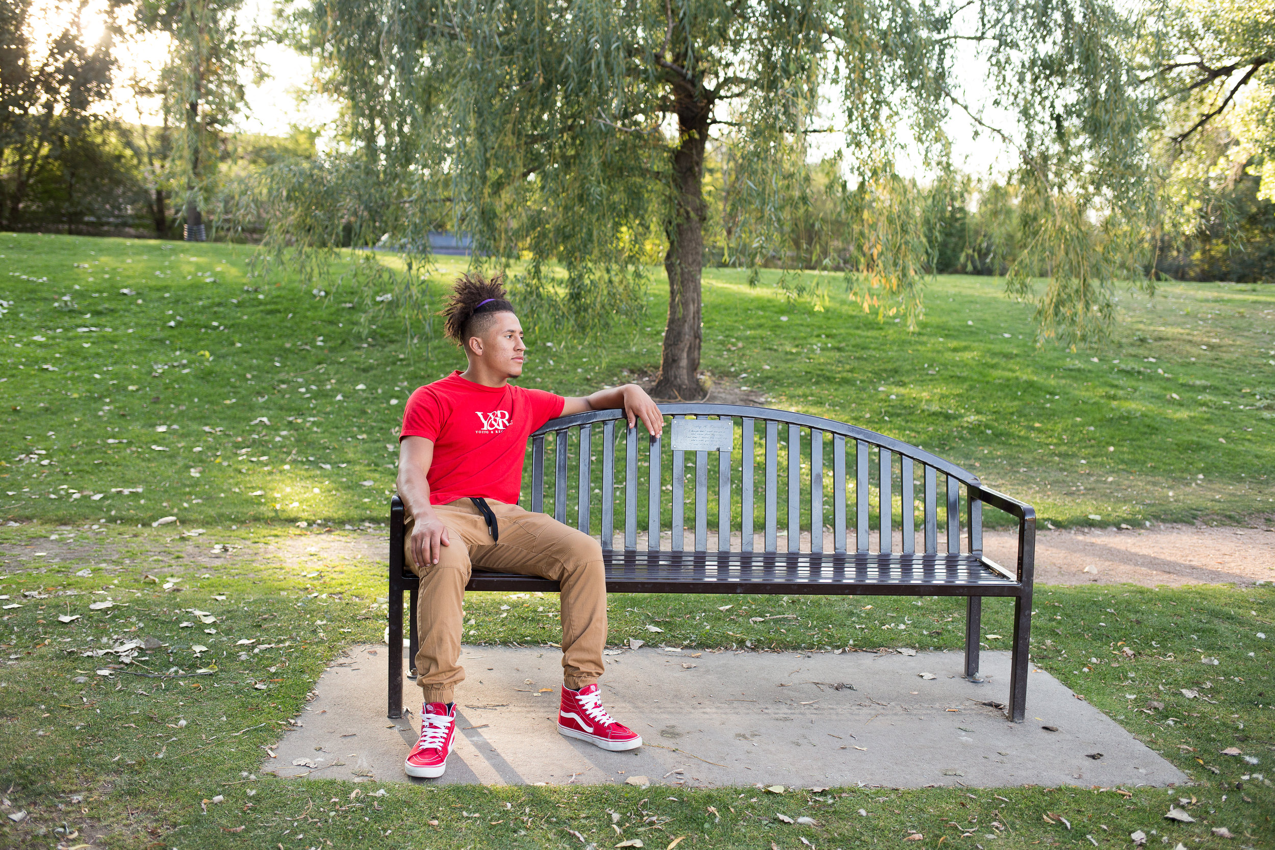 Senior sitting on the left side of a bench while looking in the distance in a red shirt in Monument Valley Park in Colorado  Springs Stacy Carosa Photography class of 2019