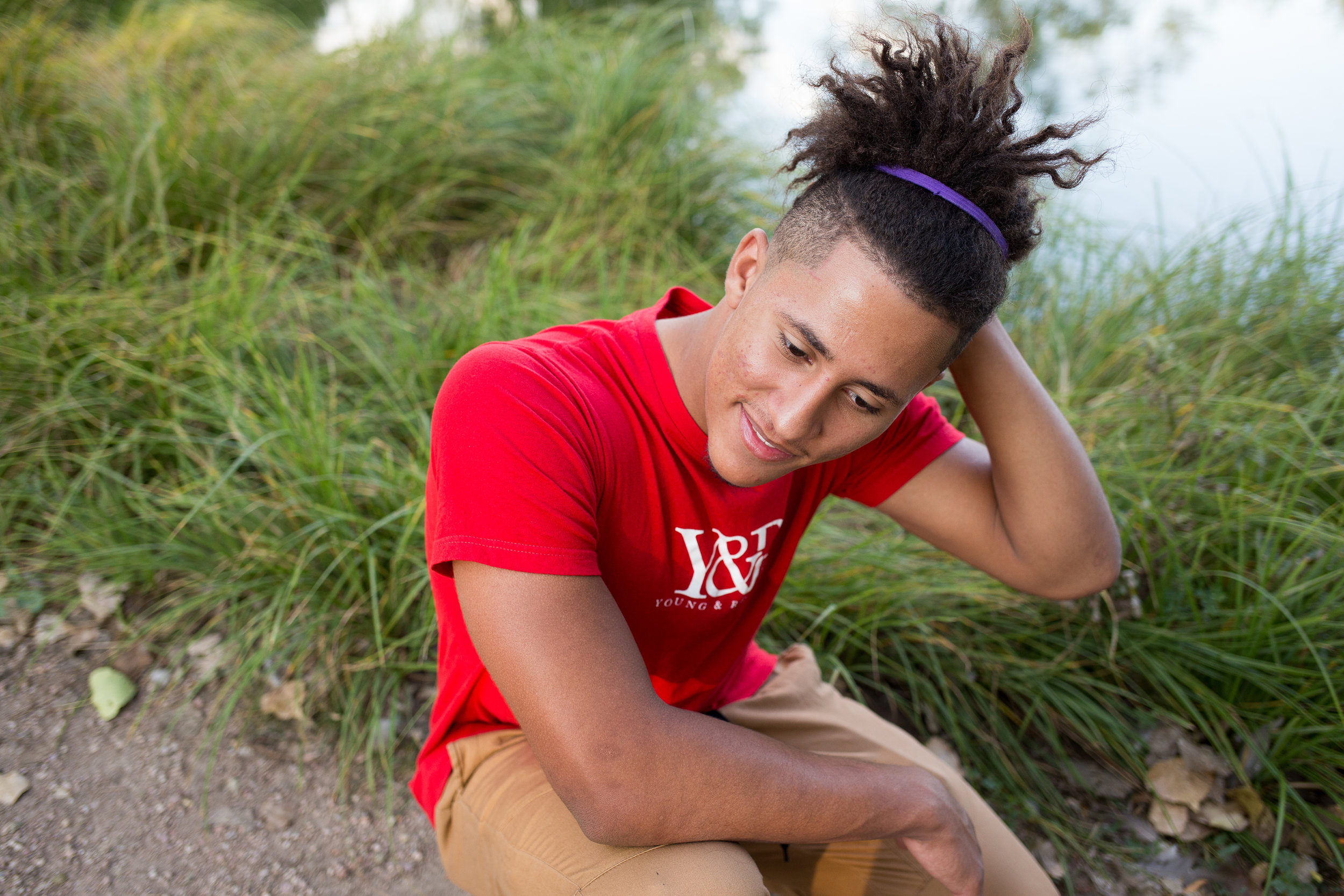 Senior boy in red shirt kneeling and looking at the ground while running his hand through his hair in Monument valley Park Stacy Carosa Photography Colorado Springs Senior Photography