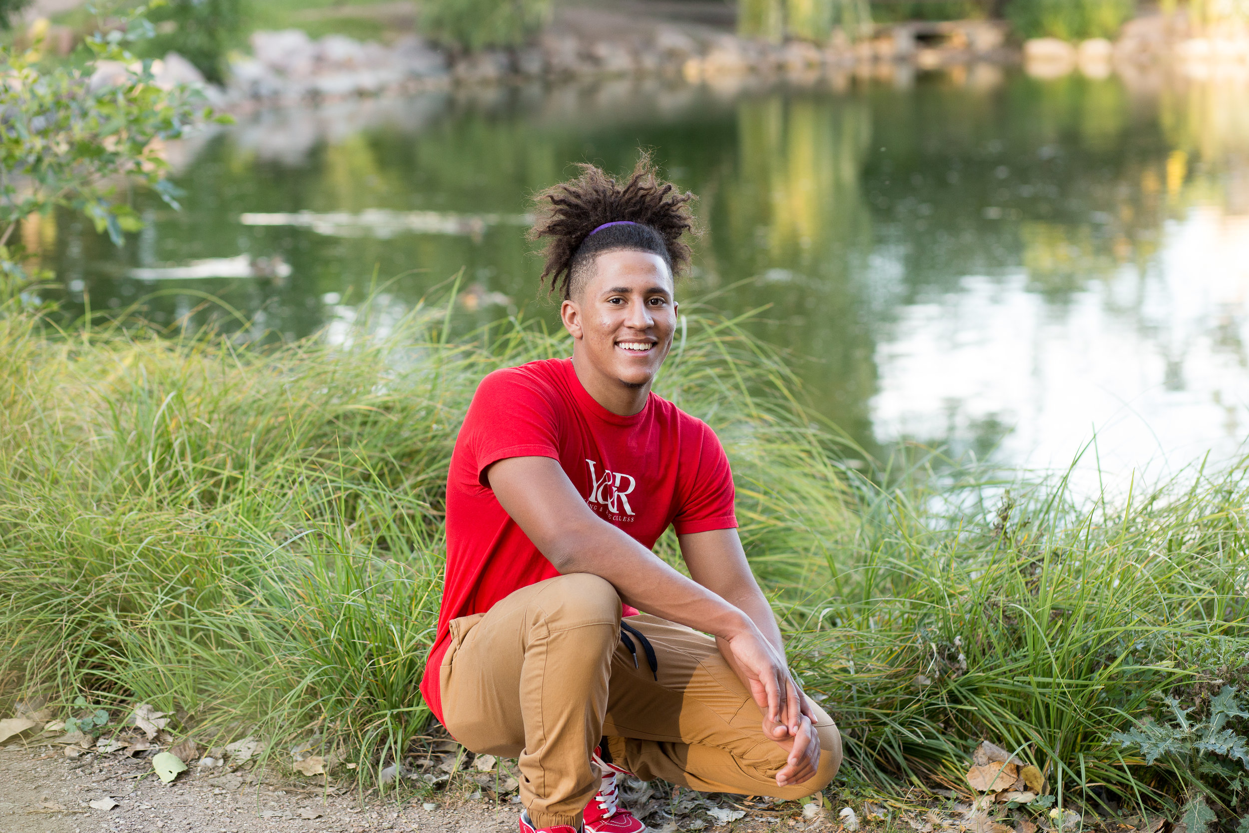 Widefield High School senior photos in Colorado Springs kneeling on a trail next to a pond in Monument Valley Park Stacy Carosa Photography
