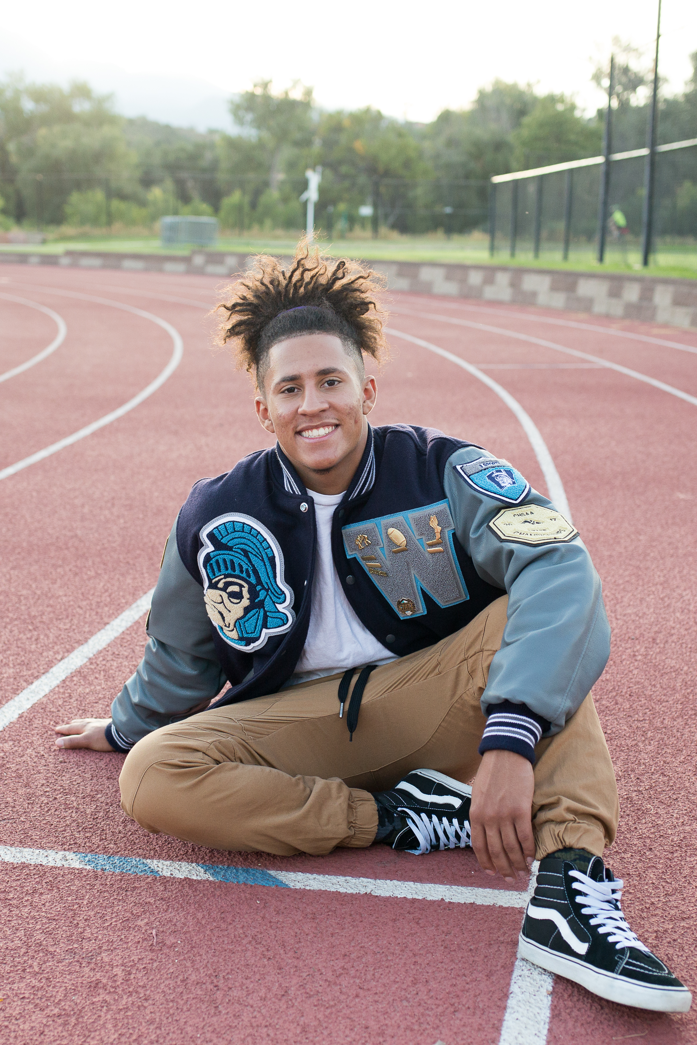 Colorado Springs Senior Photography Widefield high school senior in varsity jacket sitting on a running track